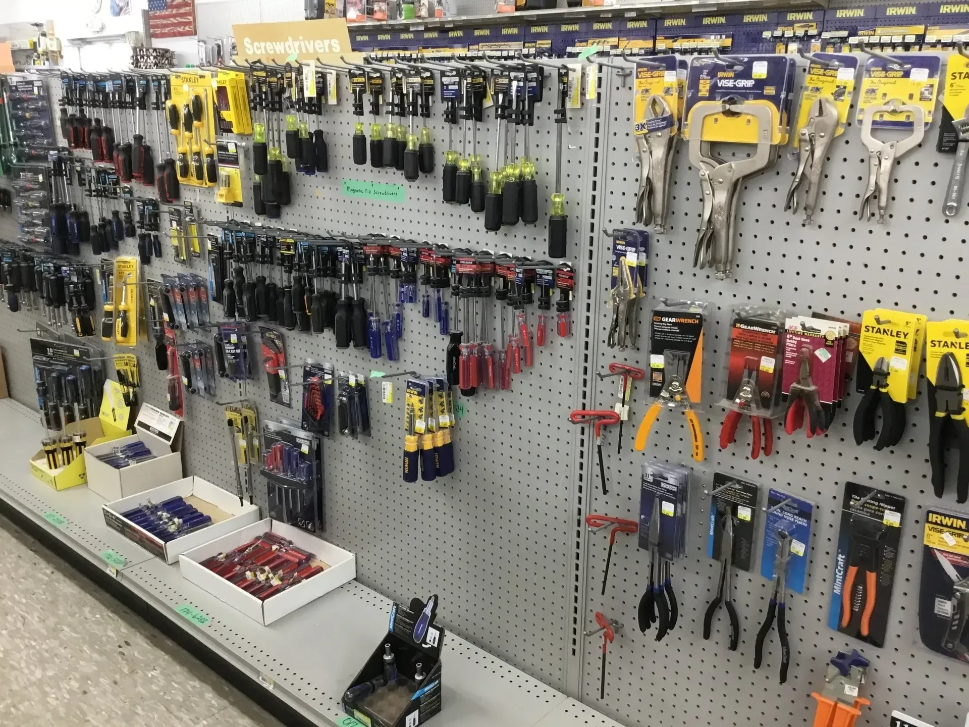 Hardware store aisle with hanging hand tools, pliers, cutters, and screwdrivers on a pegboard display.