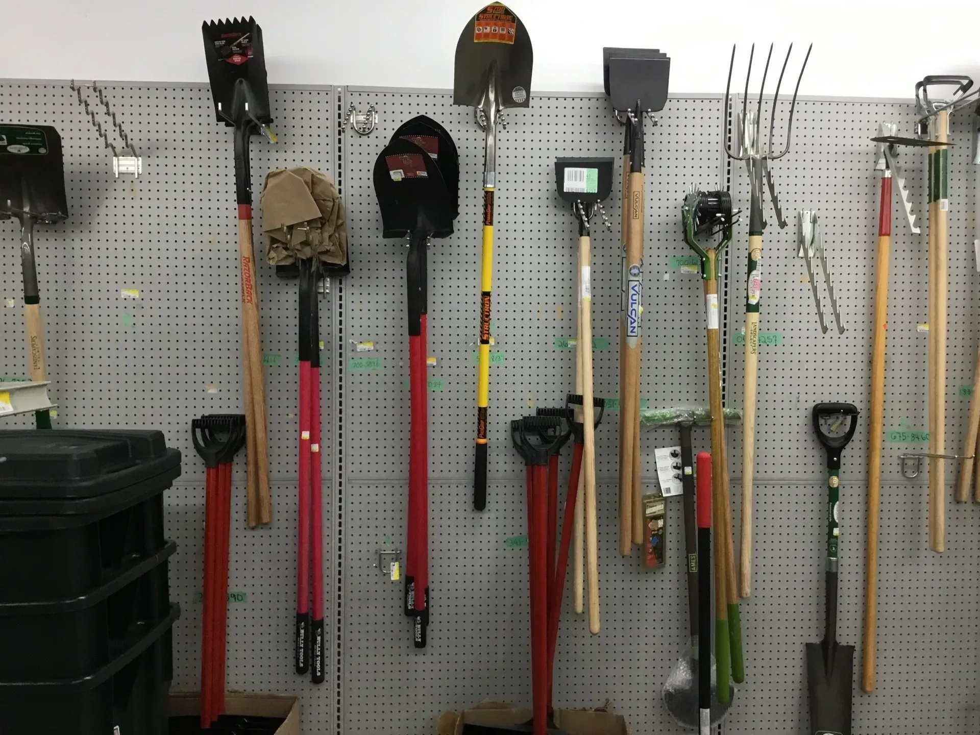 Garden tools hanging on a pegboard in a garage, including shovels, rakes, and hoes.