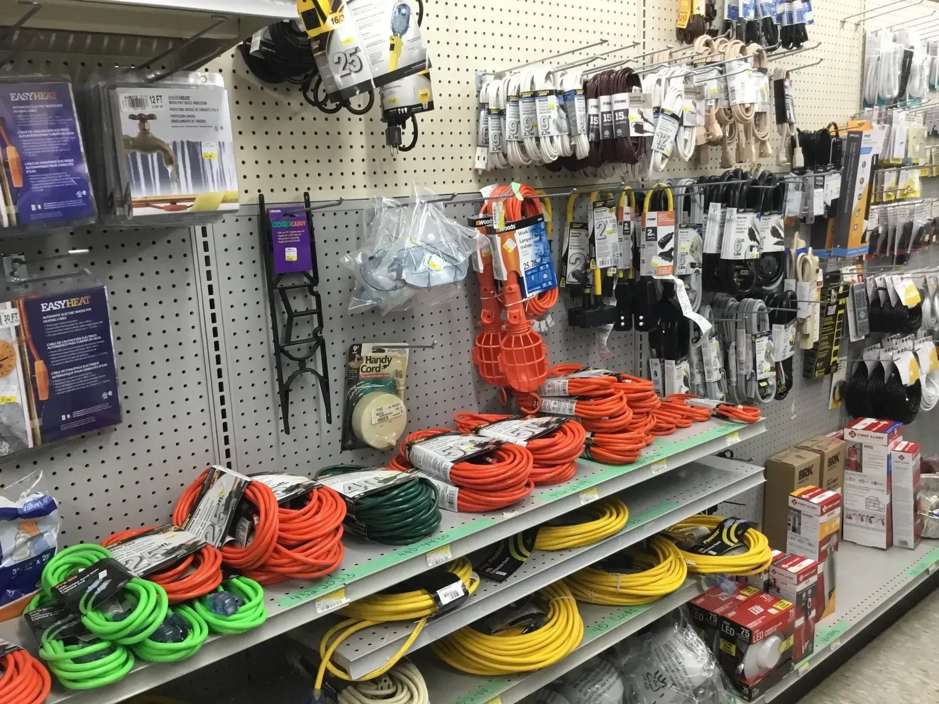 Hardware store aisle with coiled extension cords and power accessories hanging on pegboard displays.