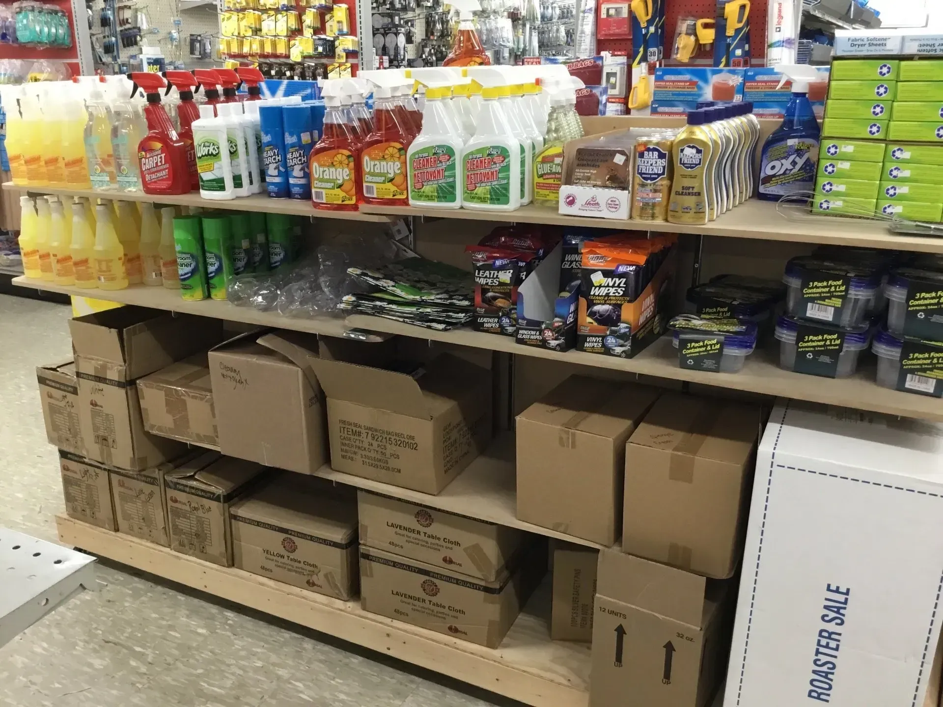 Shelves of cleaning supplies and boxed goods in a store aisle, with cardboard boxes stacked below.