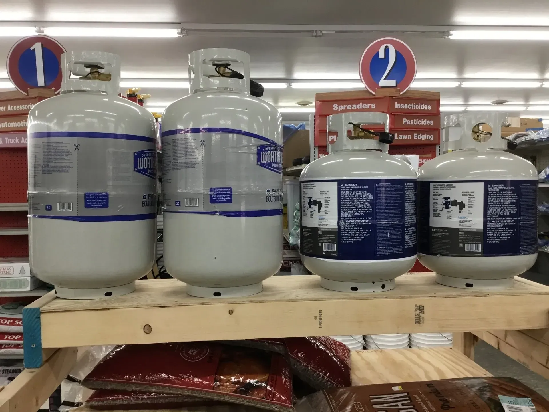 Propane tanks on a store shelf with blue-and-white labels and aisle signs 1 and 2