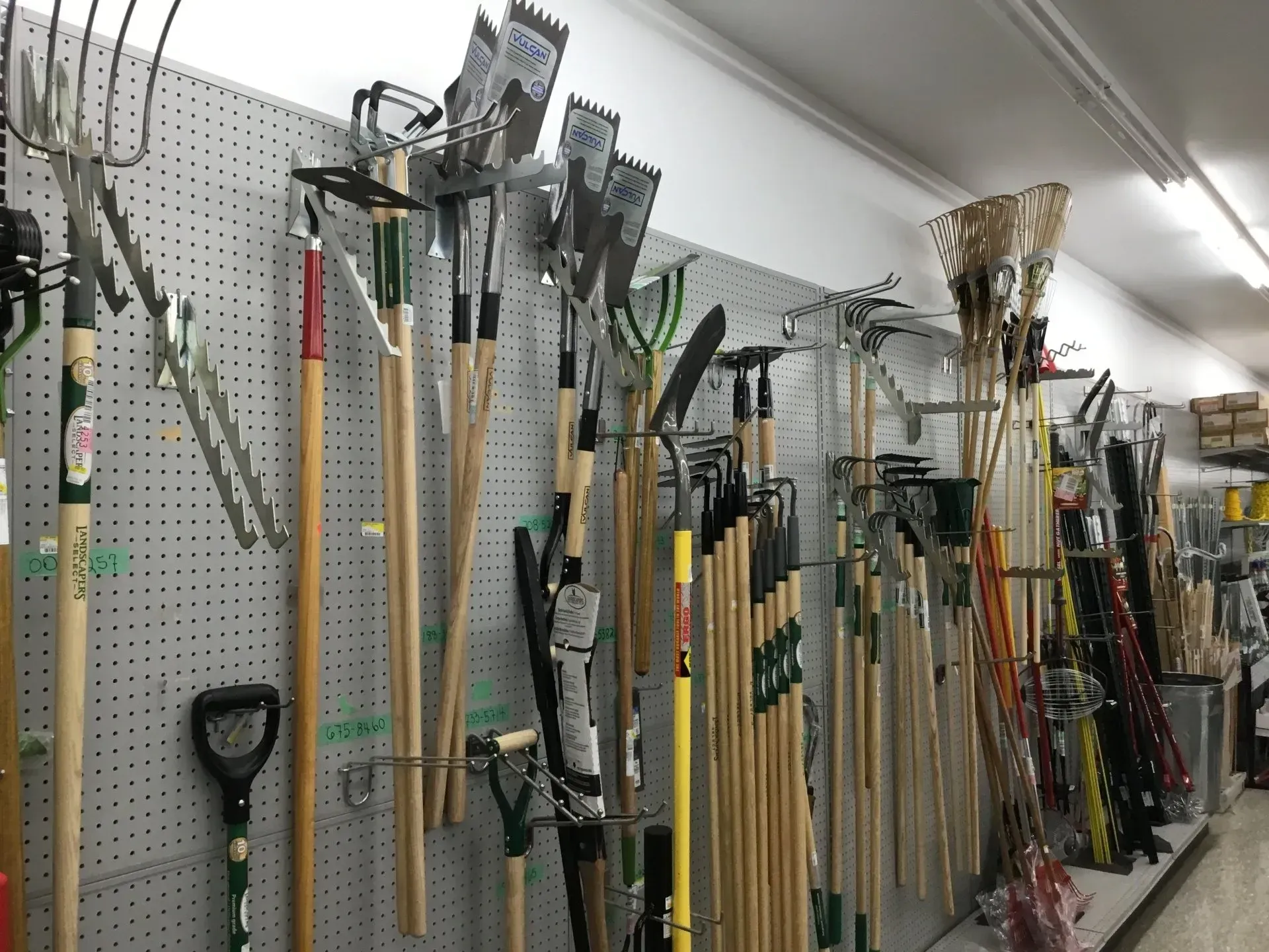 Rakes, shovels, and garden tools hanging on a pegboard wall in a store aisle
