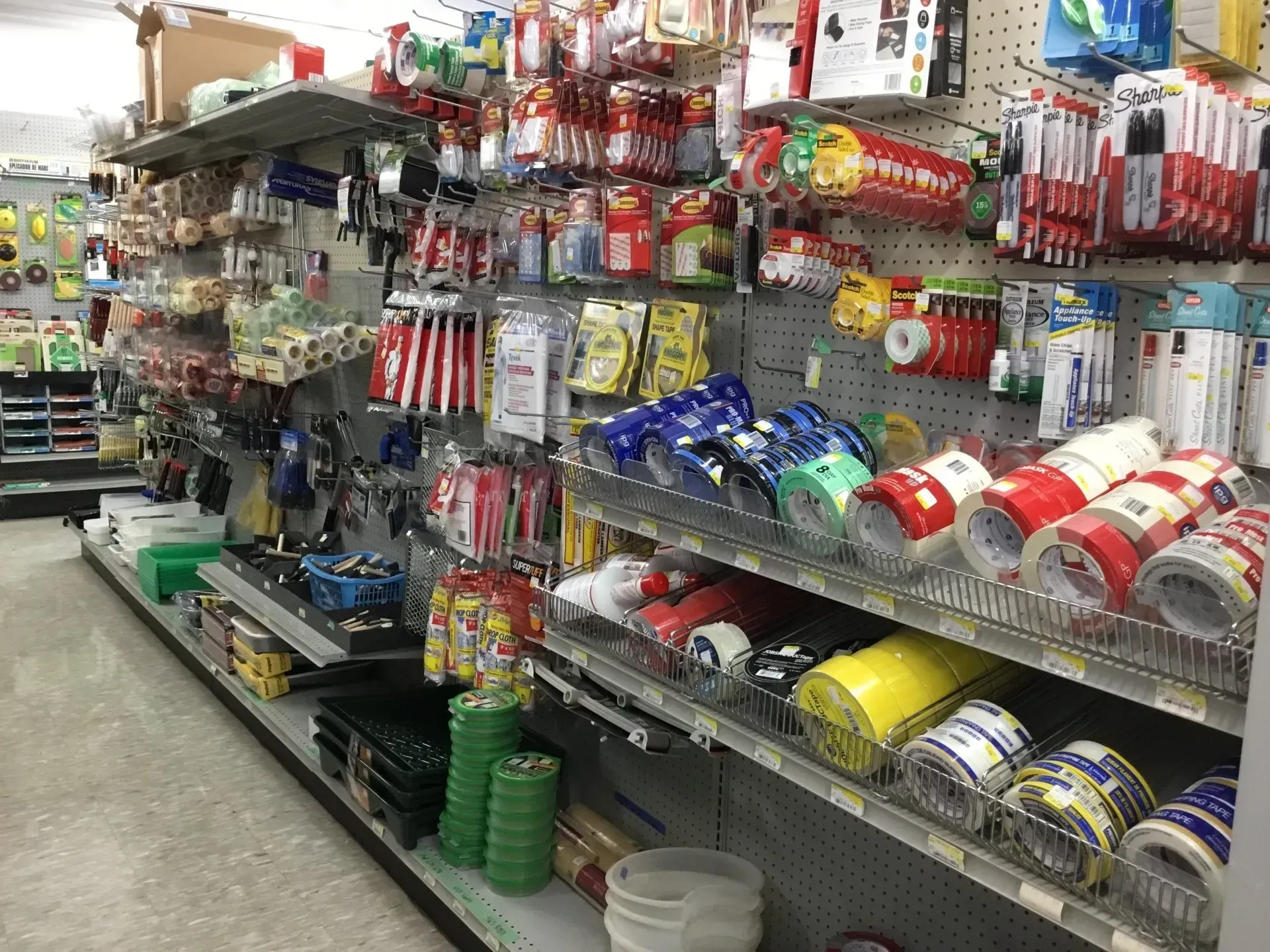 A hardware store aisle with shelves of assorted tools, tape, and supplies.