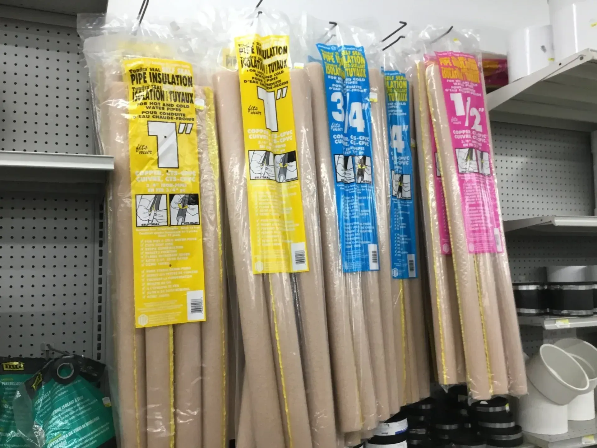Packaged wooden dowels or rods hanging on a store pegboard shelf, with yellow, blue, and pink labels.