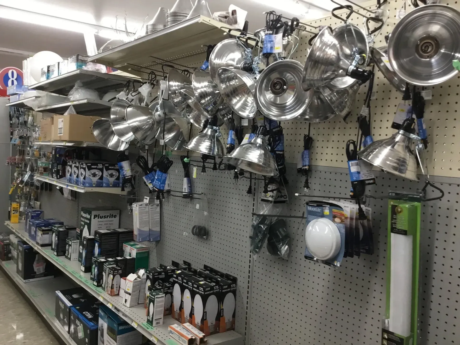 Kitchenware display wall with hanging pots, pans, utensils, and a shelf of bottles in a store.