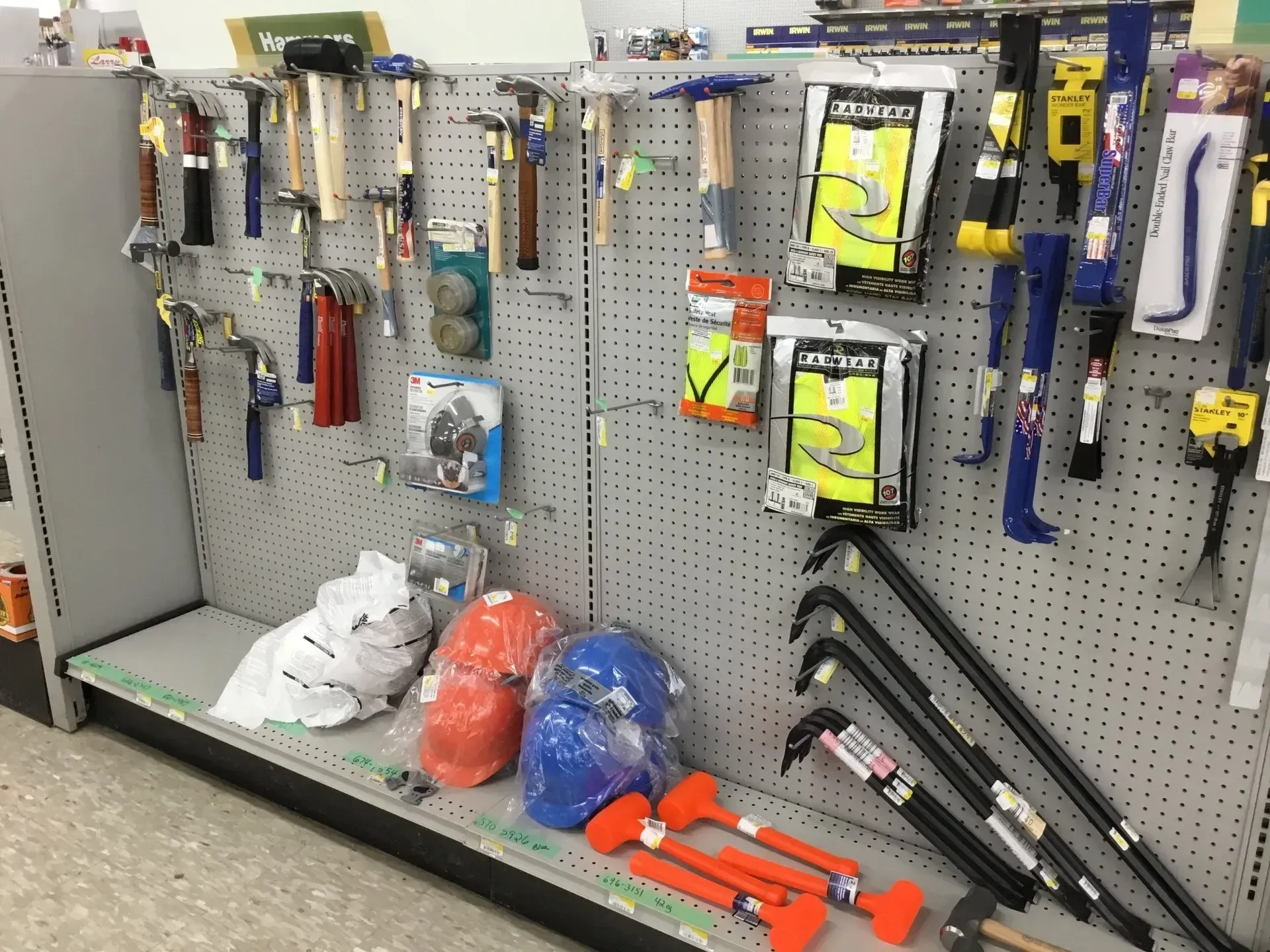 Hardware store aisle with hand tools, clamps, and safety gear displayed on a pegboard wall.