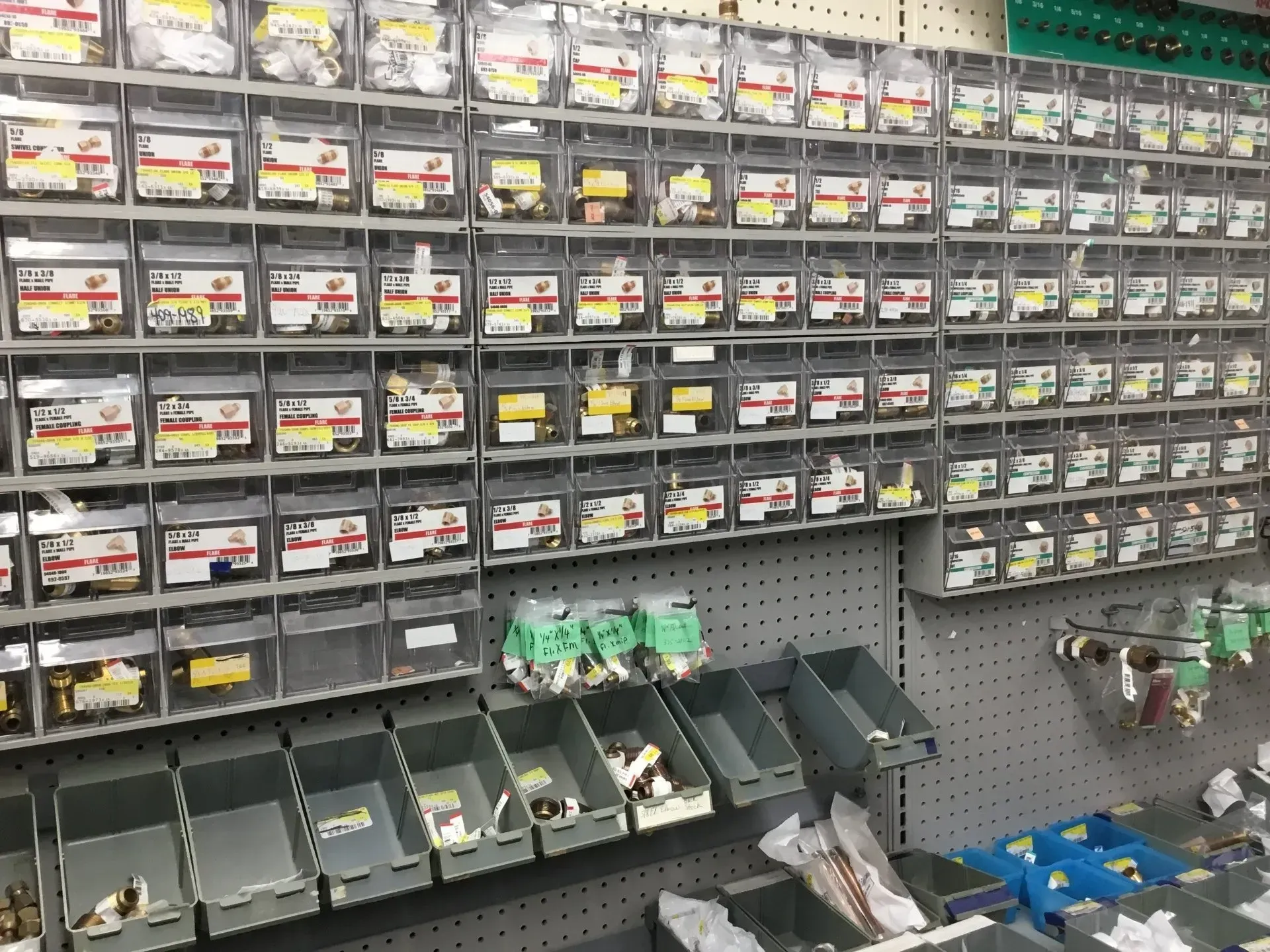 Hardware store aisle with rows of small labeled parts bins and open trays of fasteners below.