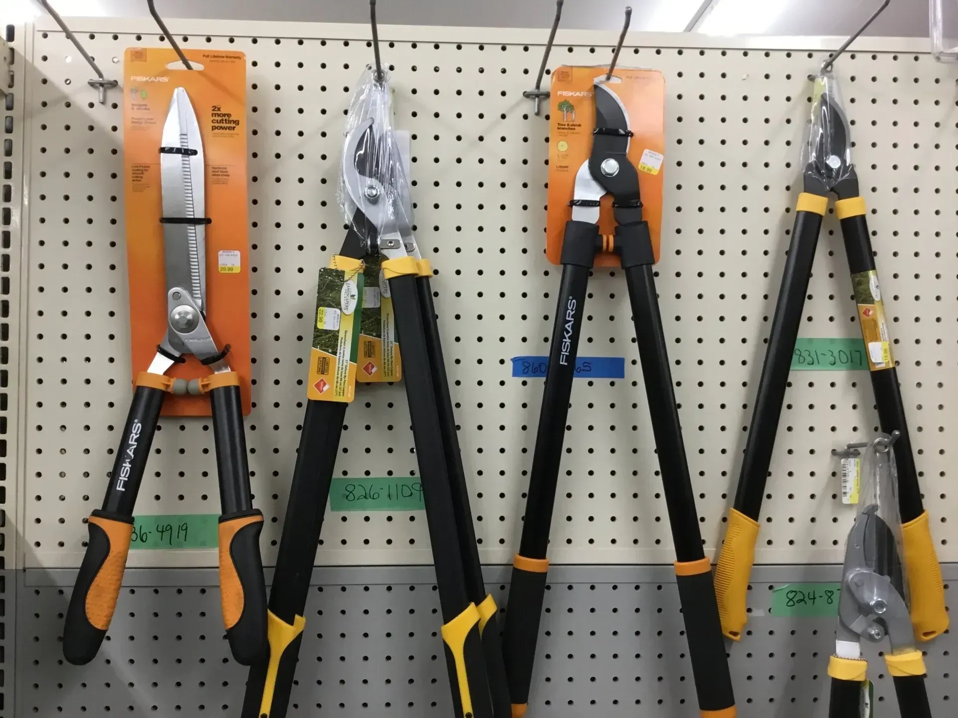 Several garden pruning loppers hanging on a pegboard display, with black handles and orange, yellow, and gray accents