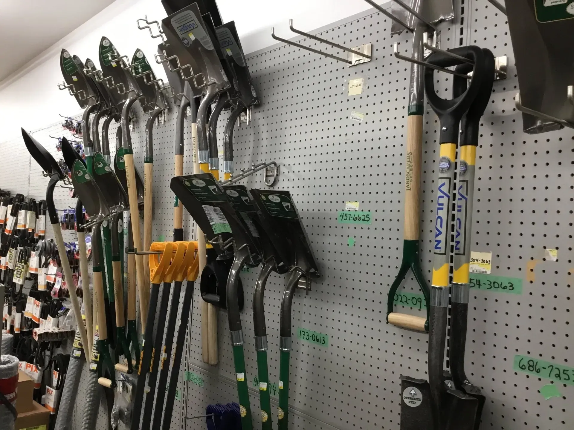 Garden tools hanging on a pegboard display in a hardware store, including shovels and rakes.