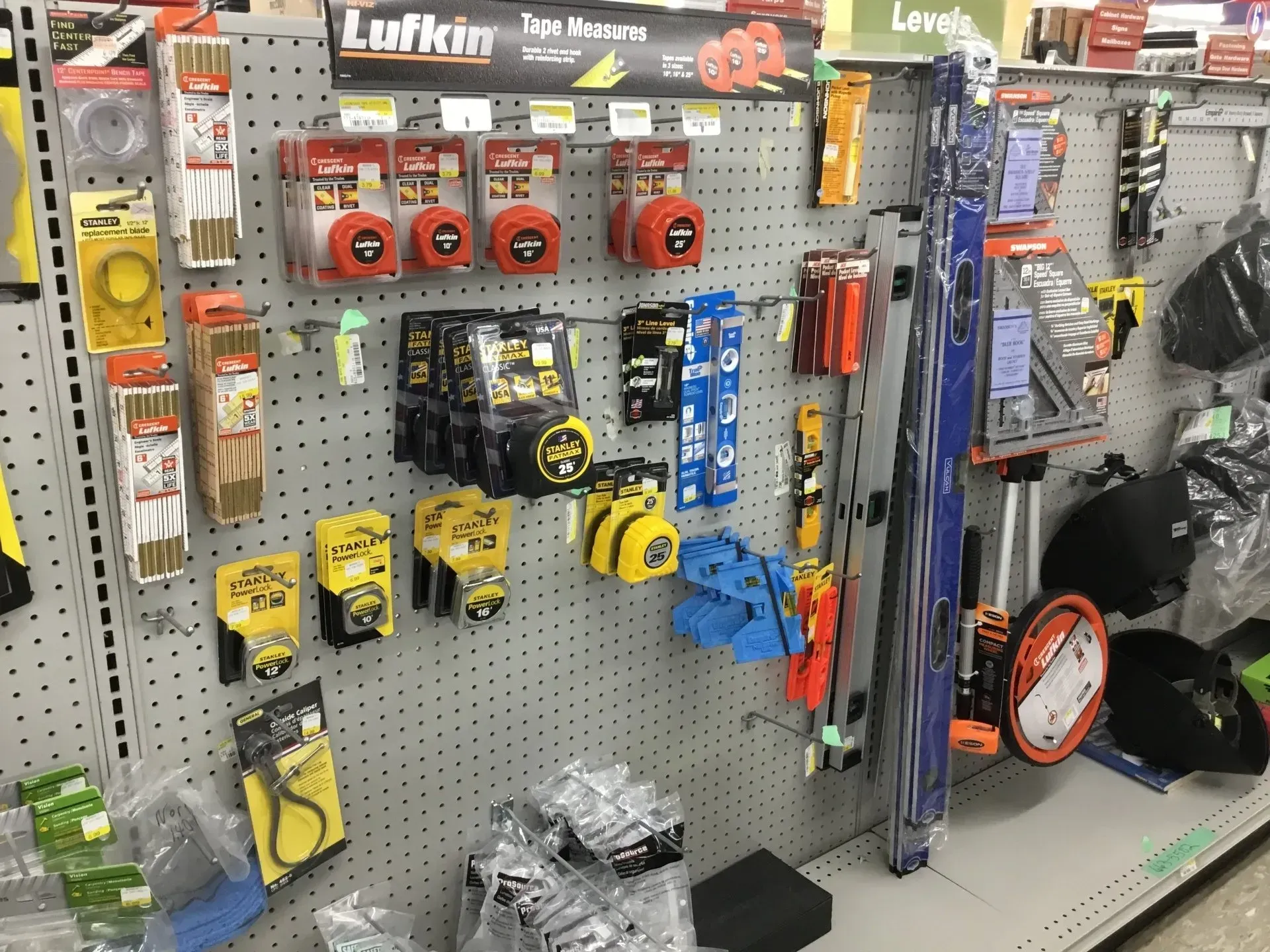 Hardware store aisle with hanging tools, tape measures, and packaged accessories on a pegboard display.