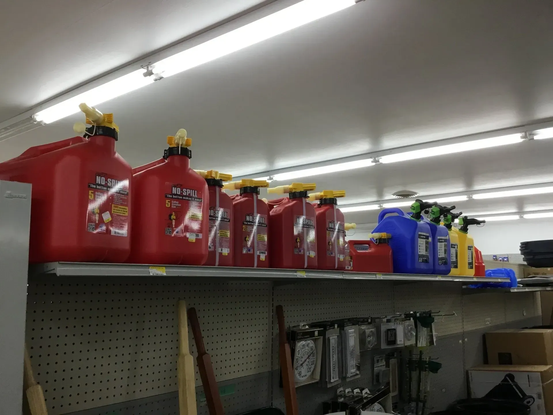 Shelf of red and blue fuel containers on a store aisle under fluorescent lights