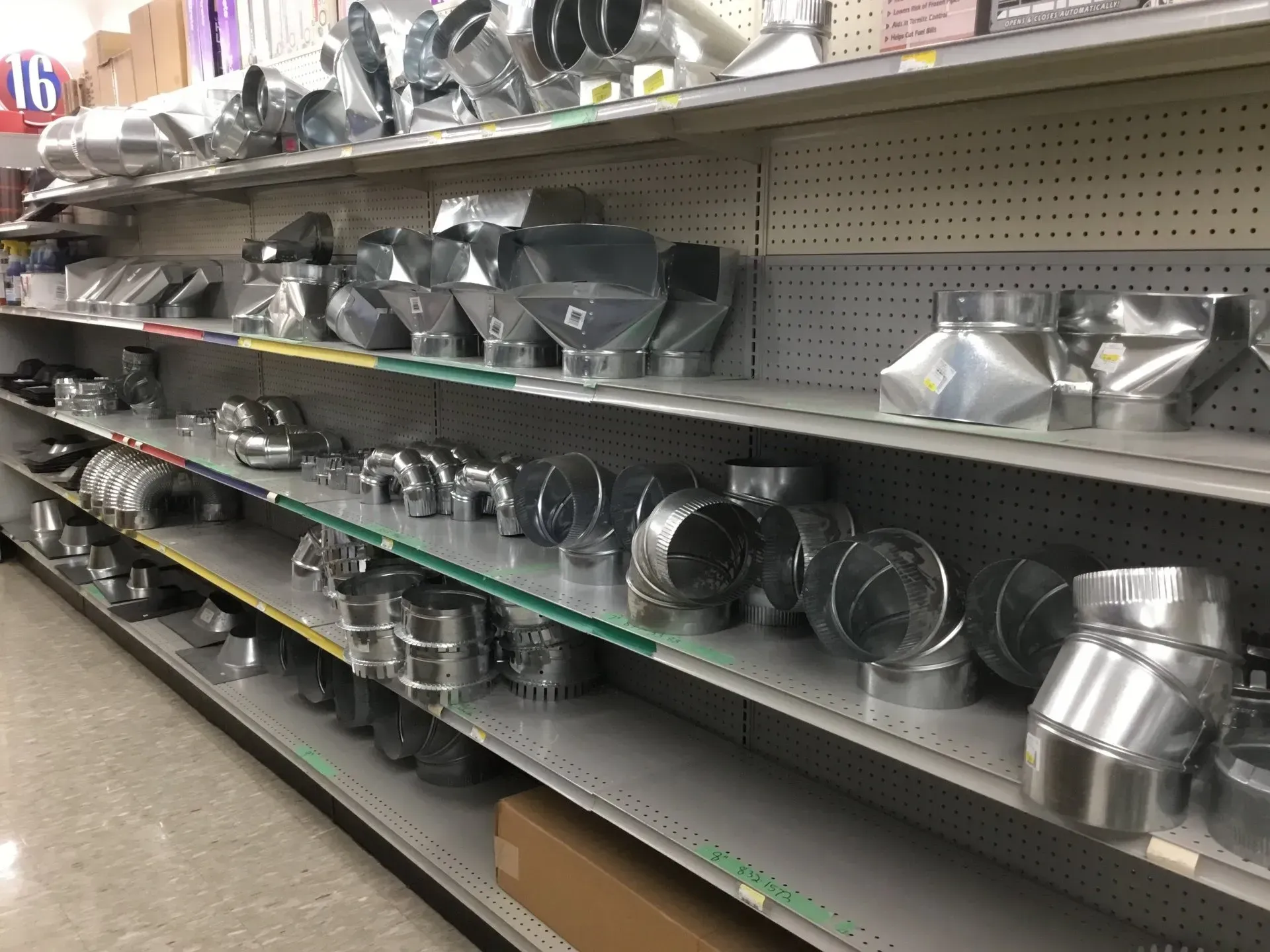 Store aisle with shelves of metal duct fittings and HVAC vents in a hardware store.