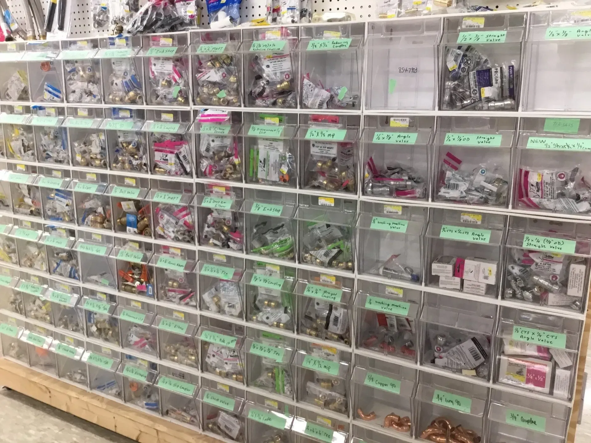 Rows of clear storage bins filled with small toy vehicles, with green labels on a shelf.