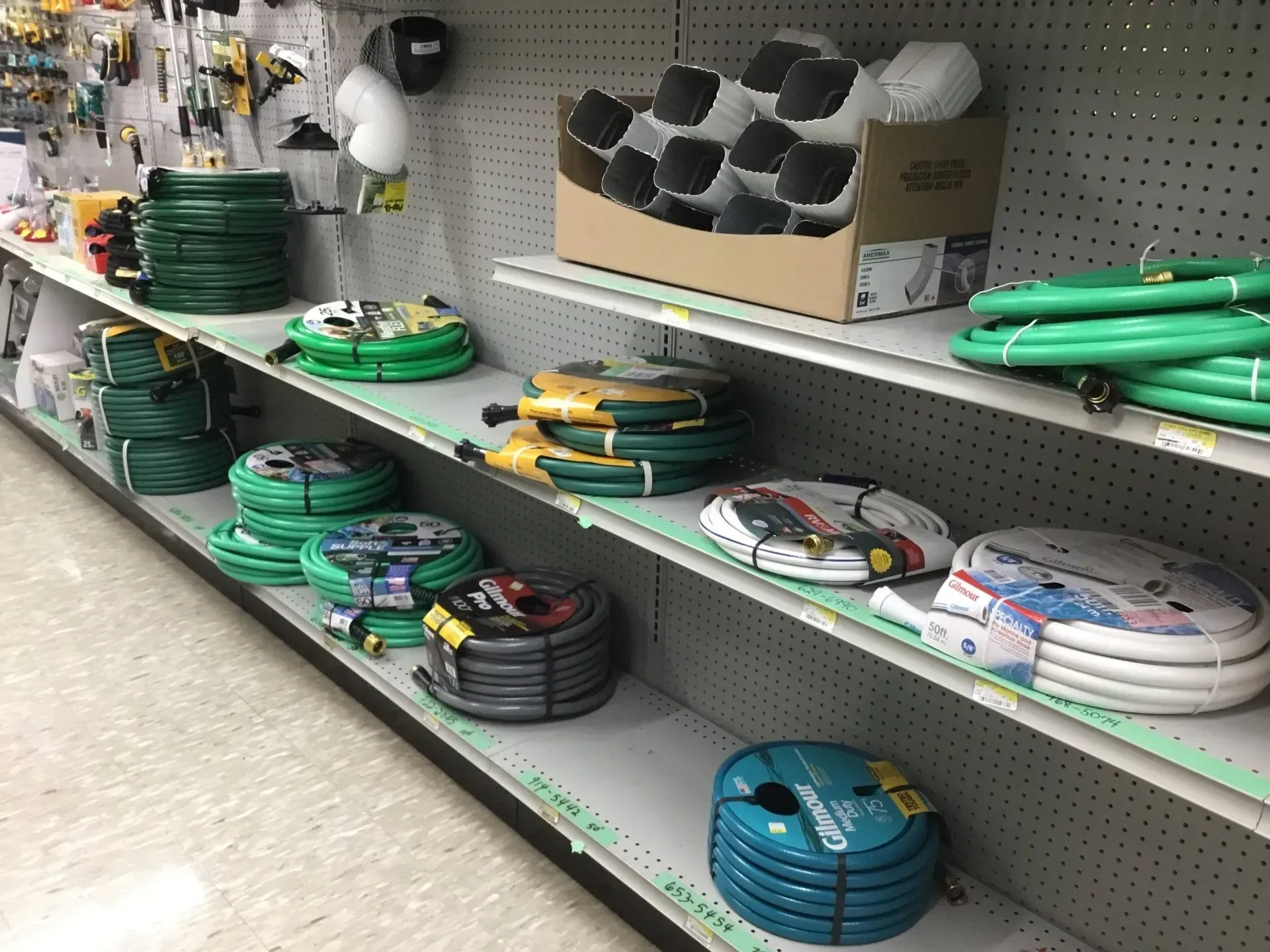 Hardware store aisle with coiled garden hoses and nozzles on metal shelves