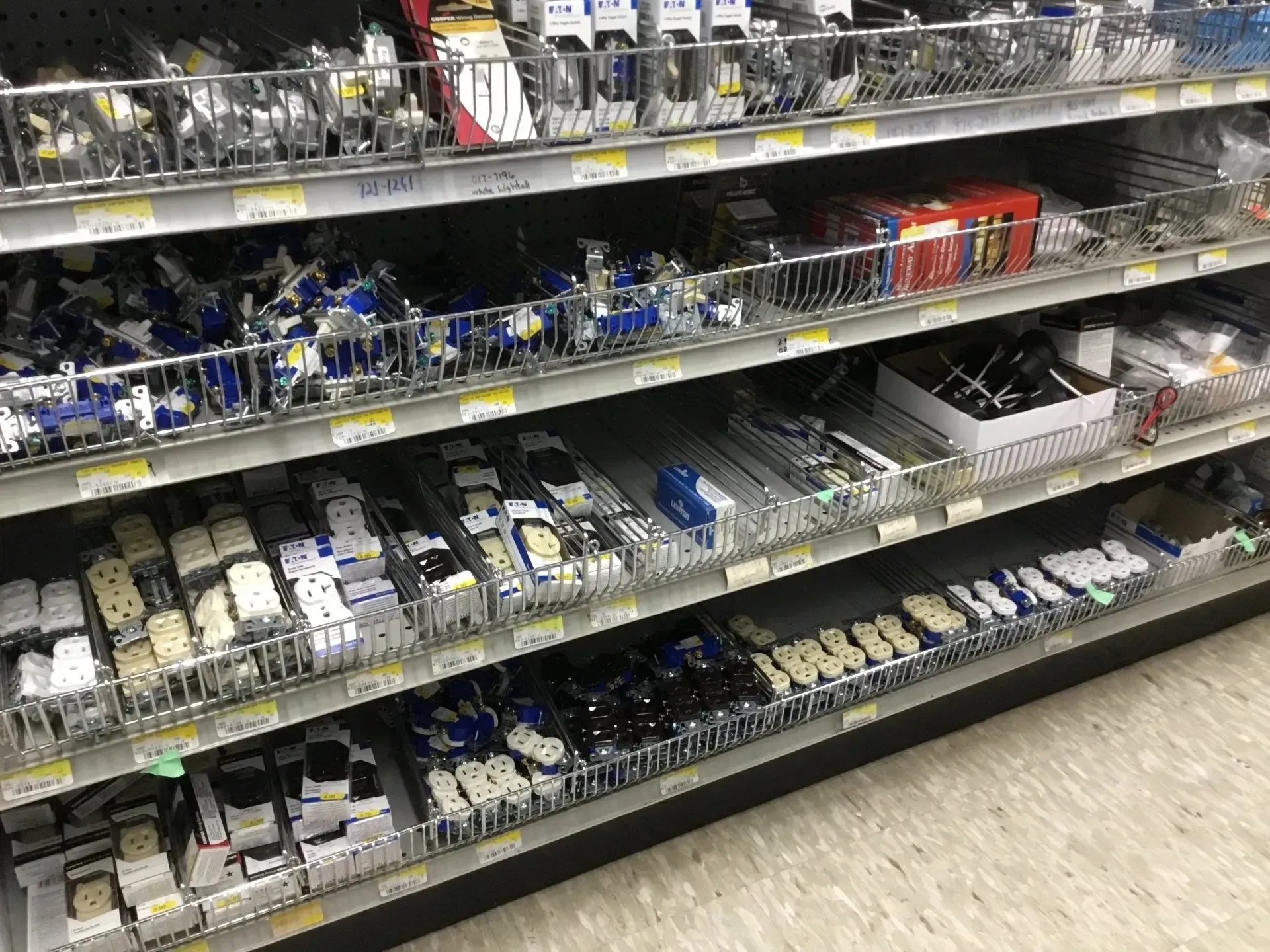 Store aisle with shelves of assorted packaged hardware items in white, blue, and black.