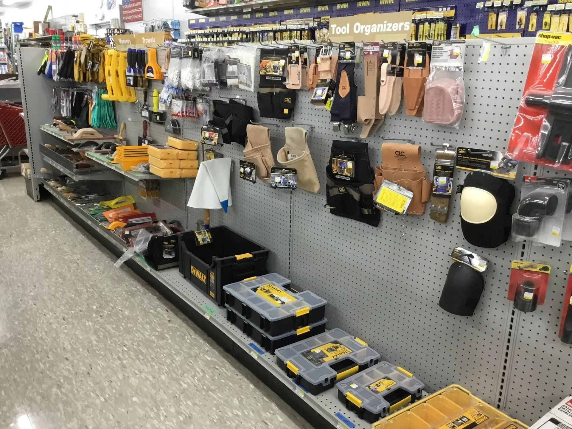 Hardware store aisle with hanging tools, bins, and packaged accessories on a pegboard display.