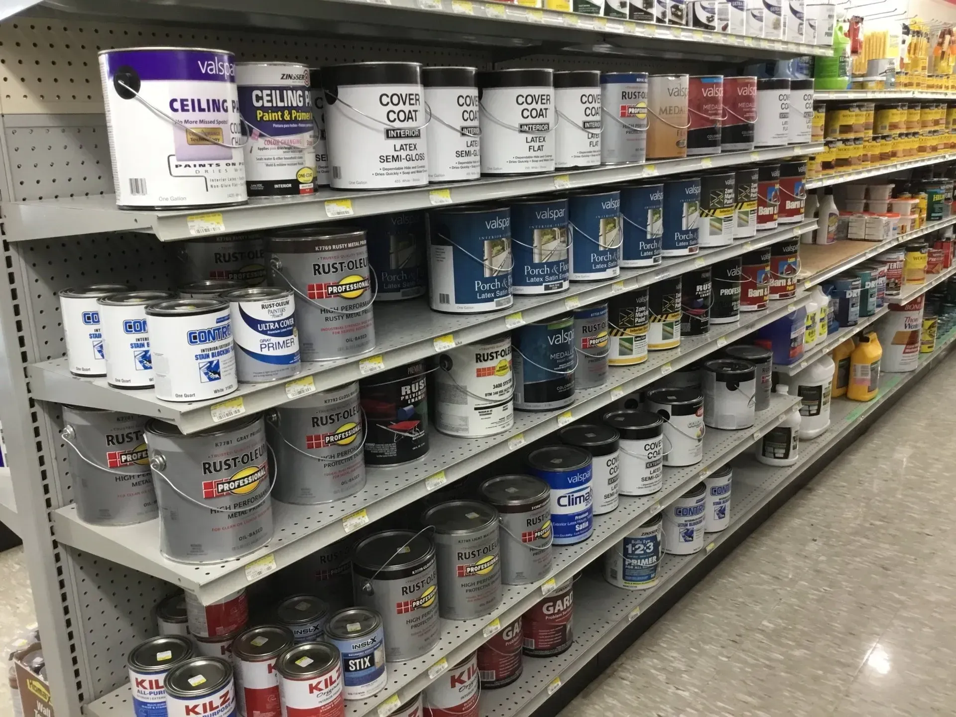 Paint cans stacked on shelves in a hardware store aisle.