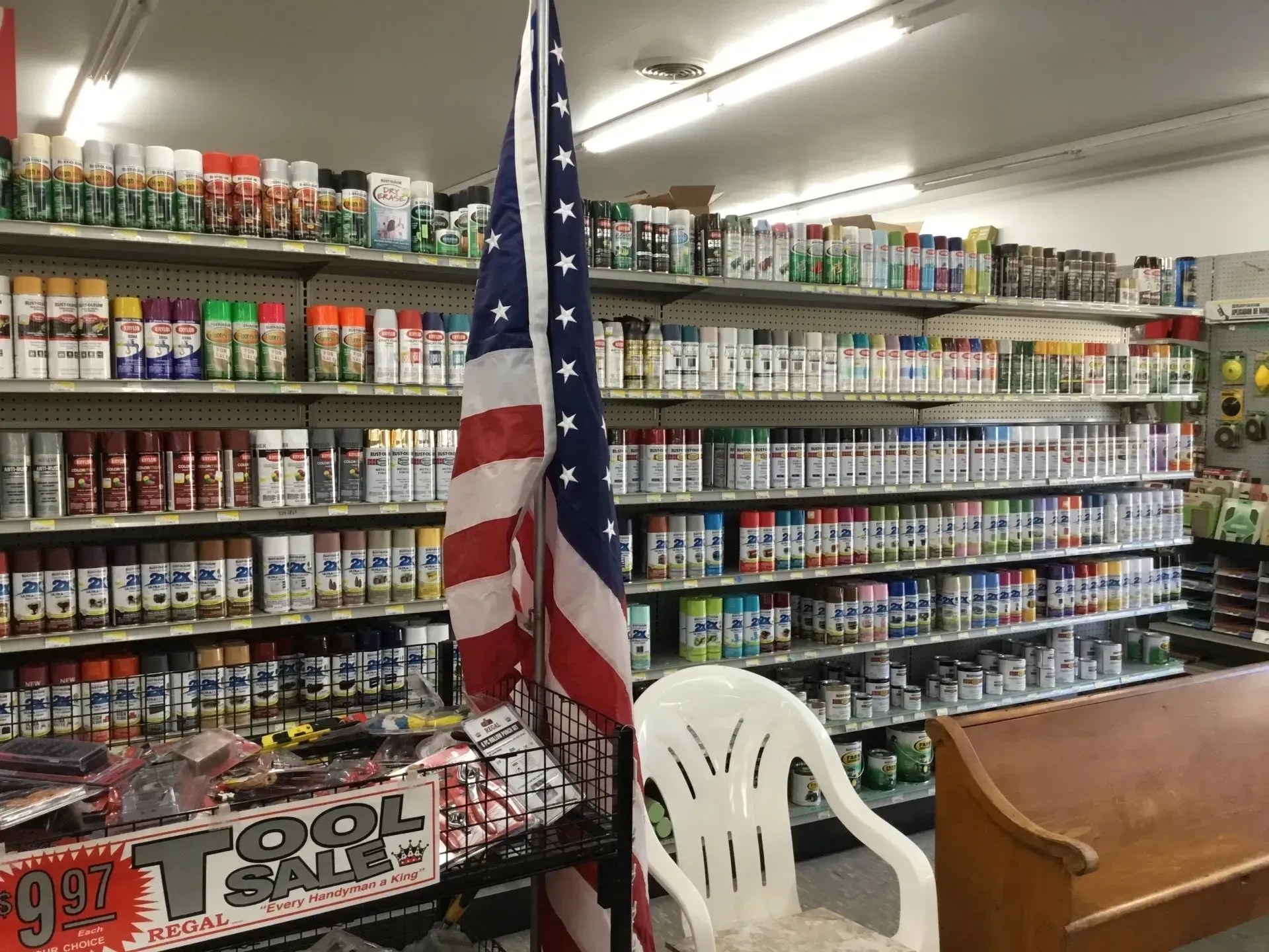 American flag in a store aisle with shelves of bottled goods and a white chair in the foreground