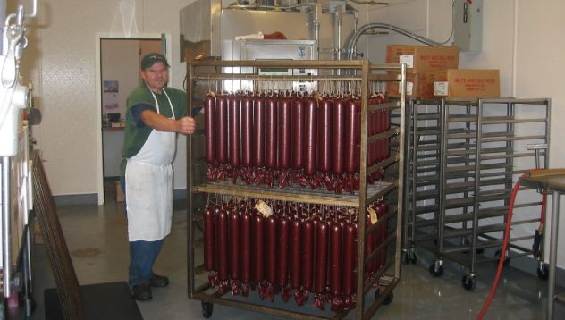 Man in apron pushing a cart of smoked sausage in a processing room