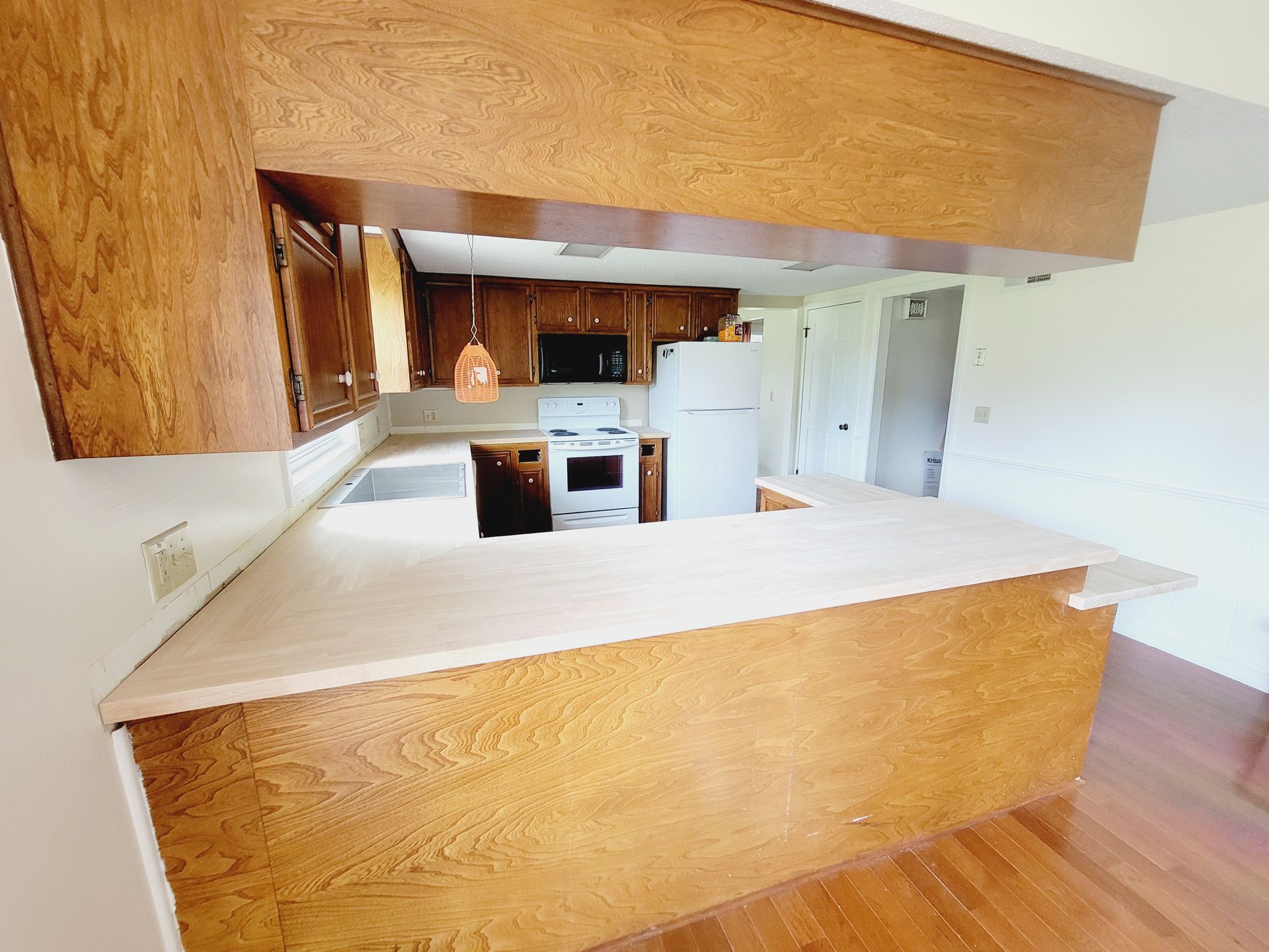 Kitchen with wooden cabinets, countertop, and appliances. View through an open pass-through.