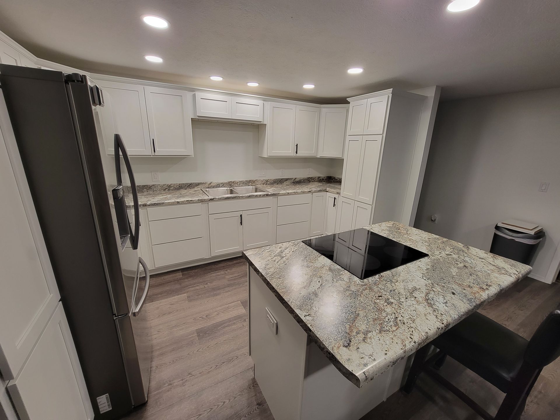 White kitchen with granite countertops, island with cooktop, and stainless steel appliances.
