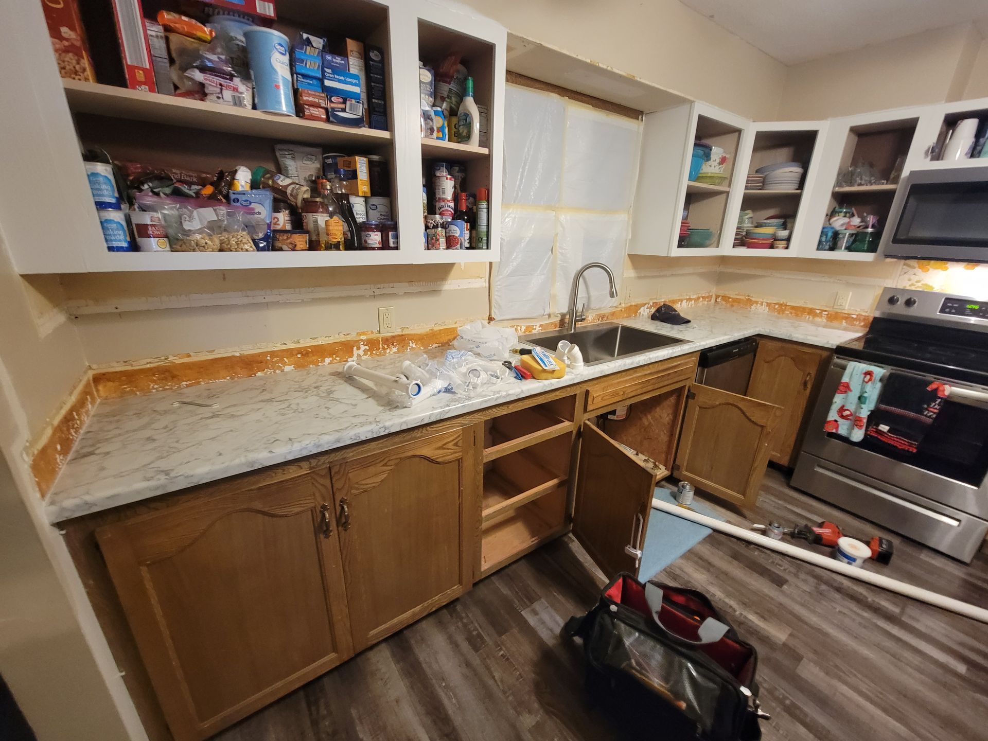 Kitchen undergoing renovation; wooden cabinets, light countertops, open cabinets, sink, and stove.