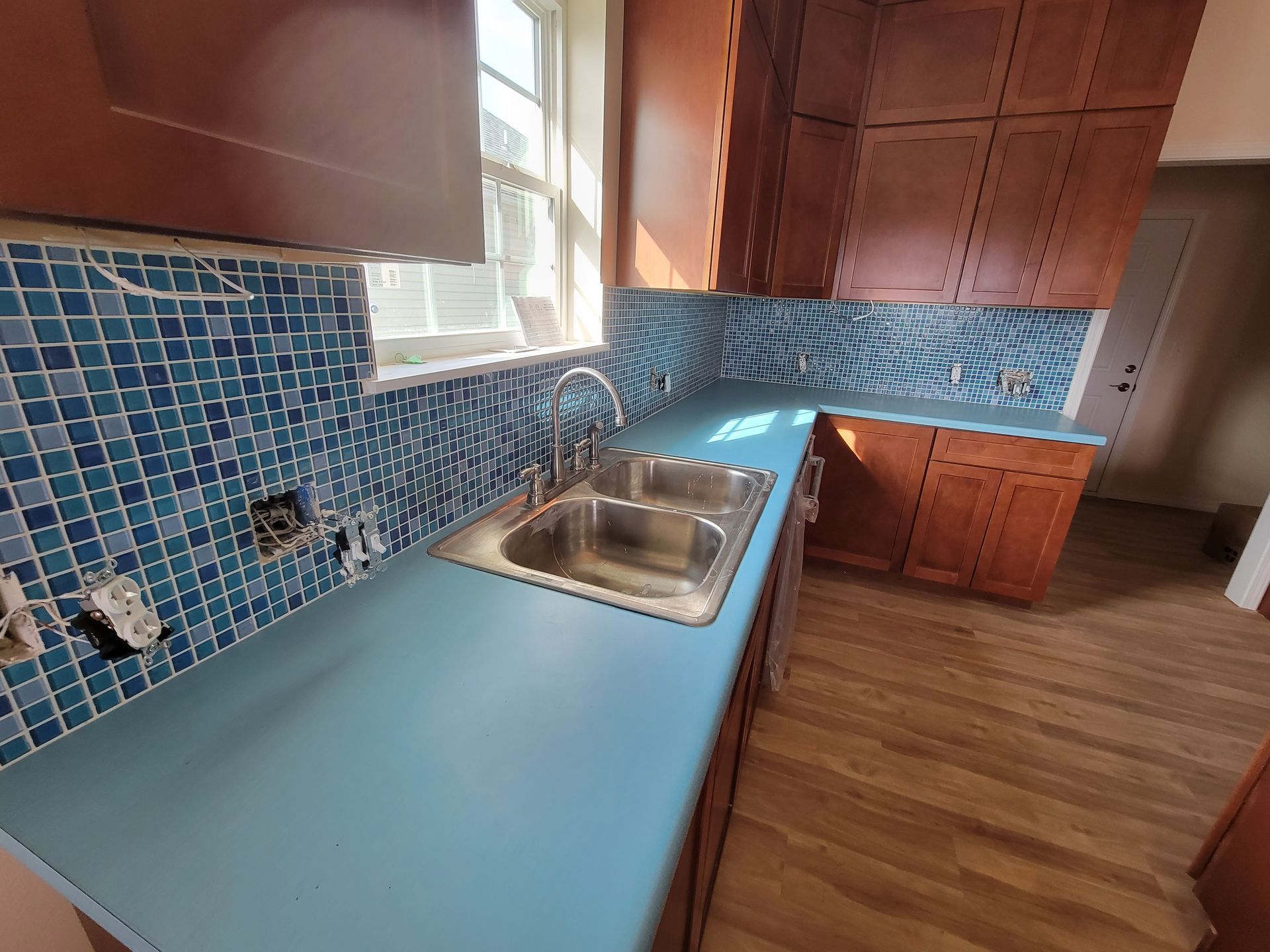 Kitchen with blue countertop, sink, blue tile backsplash, and wood cabinets.