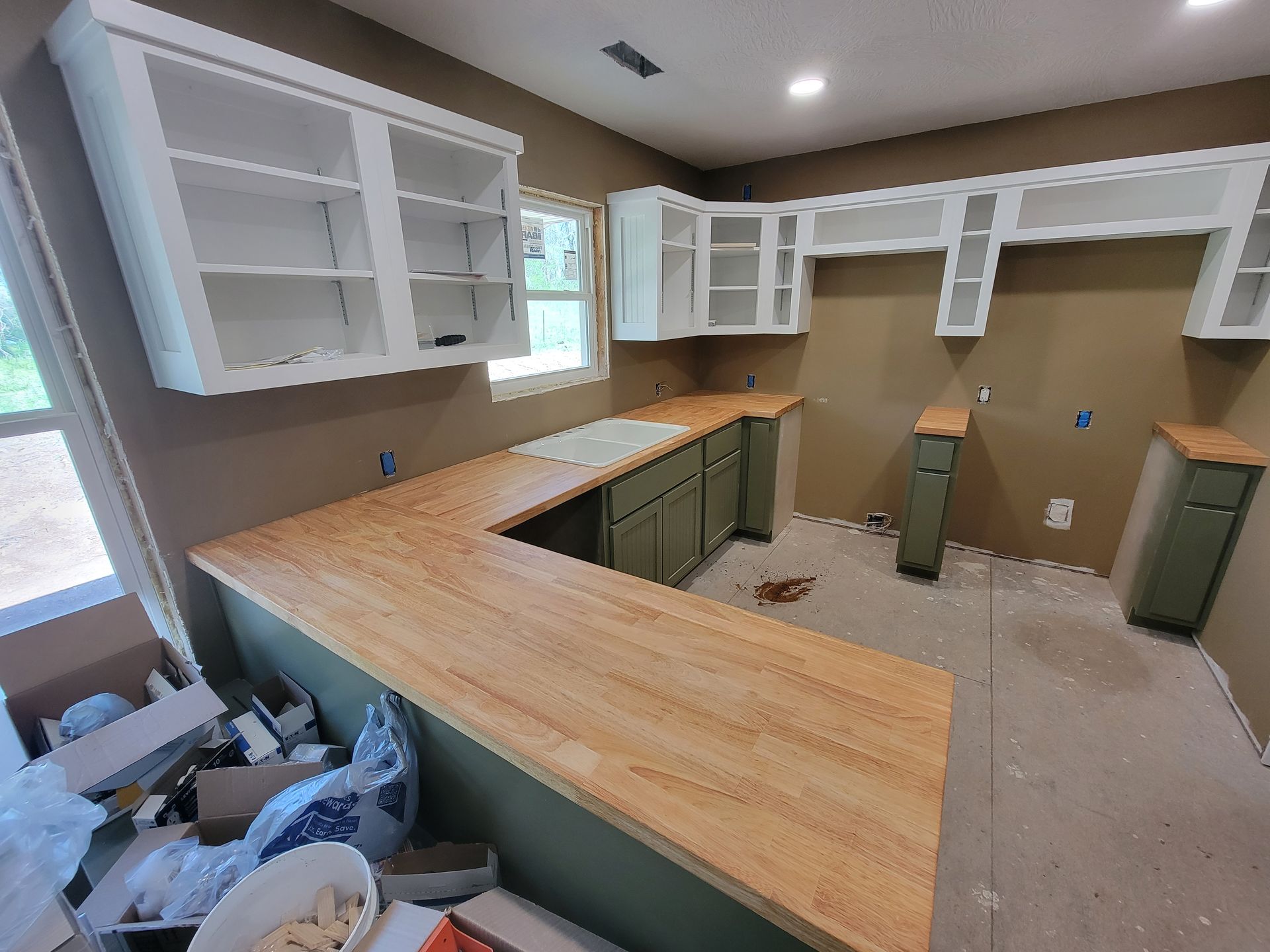 Kitchen under construction with green cabinets, wood countertops, and white upper cabinets.