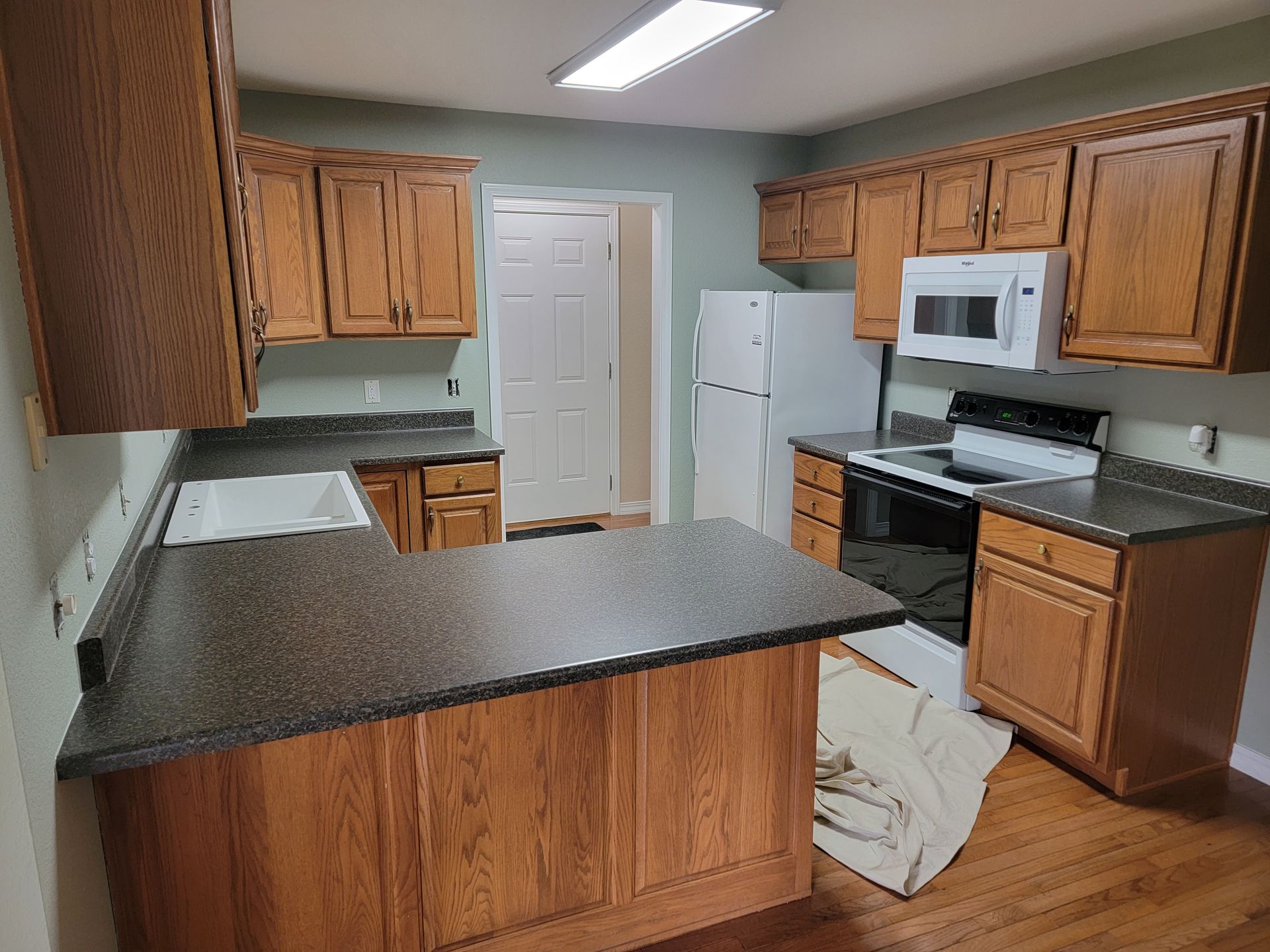 A kitchen with wooden cabinets, dark countertops, a white refrigerator, and a microwave above a stove.