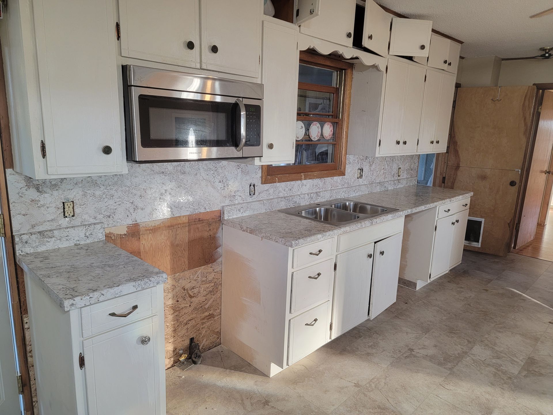 White kitchen cabinets with granite countertops, stainless steel microwave and sink, and unfinished drywall.