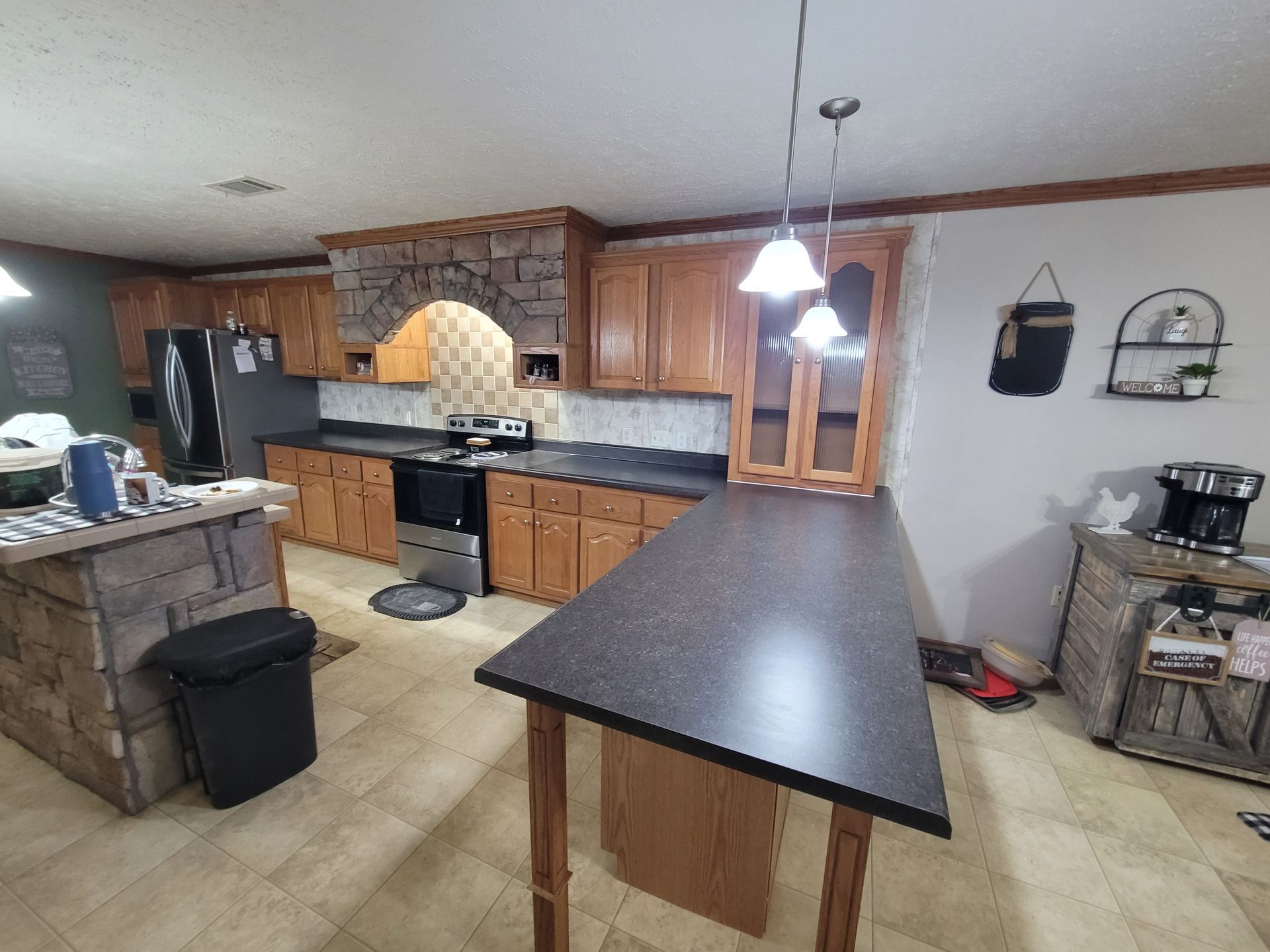 Kitchen with wood cabinets, dark countertops, a stone-like island, and two pendant lights.