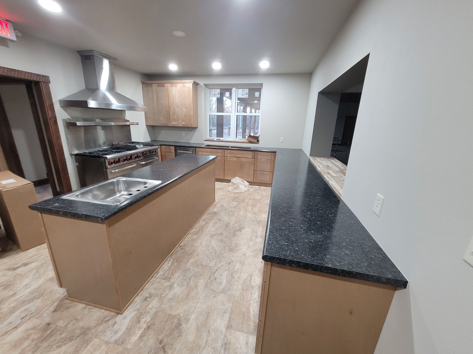 Kitchen with stainless steel appliances, dark countertops, wood cabinets, and a long island.