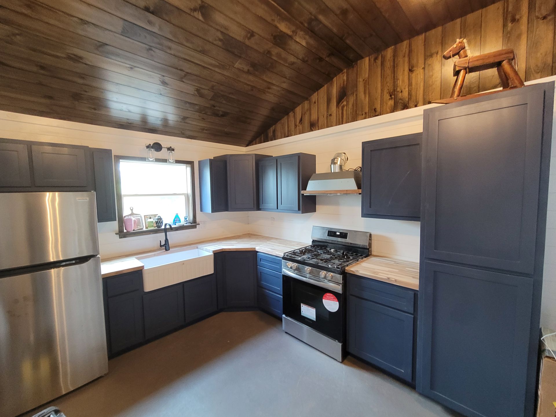 Kitchen with dark blue cabinets, stainless steel appliances, and wood ceiling.