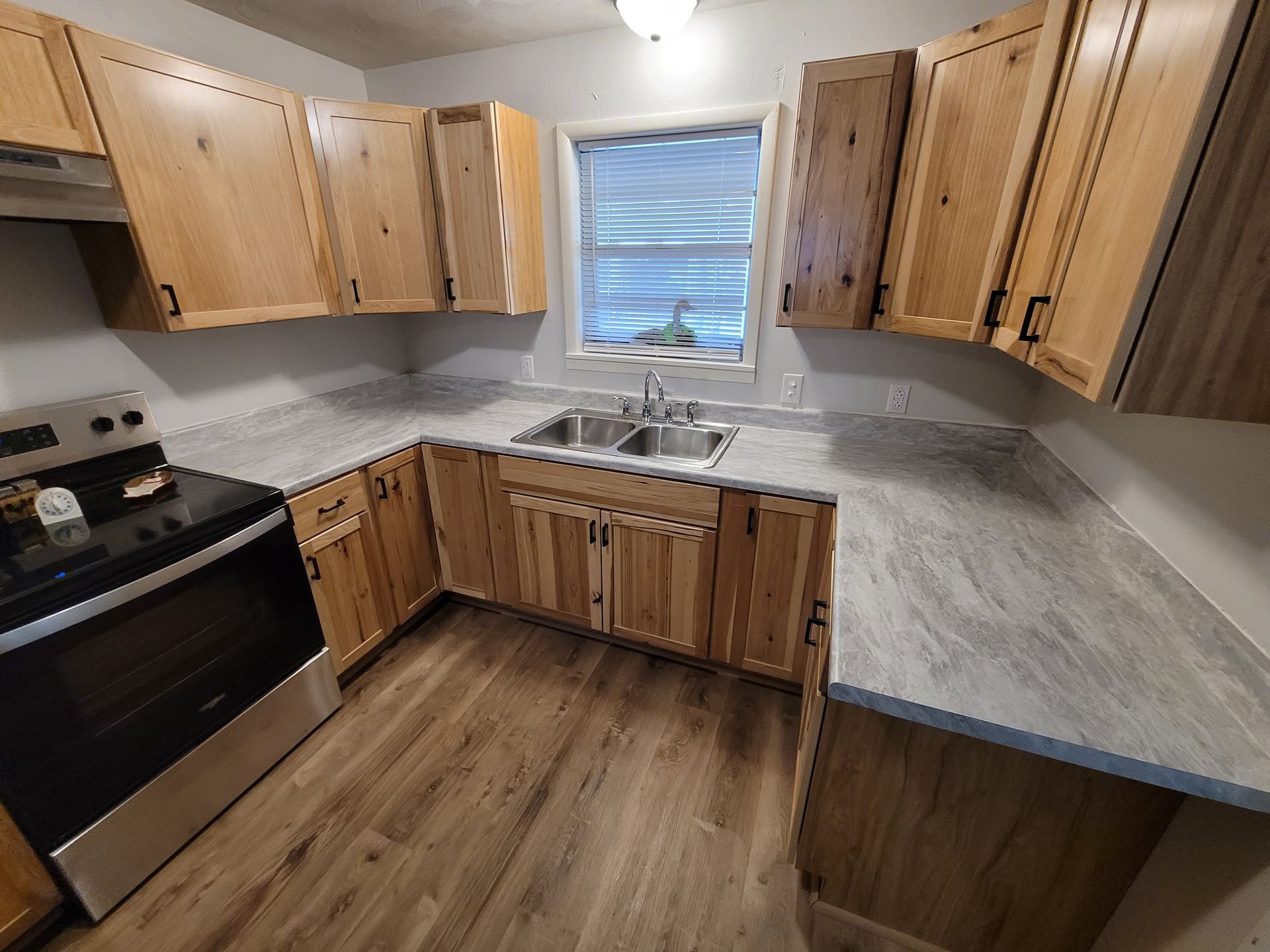 Kitchen with light wood cabinets, gray countertops, a stainless steel stove, and a window above the sink.