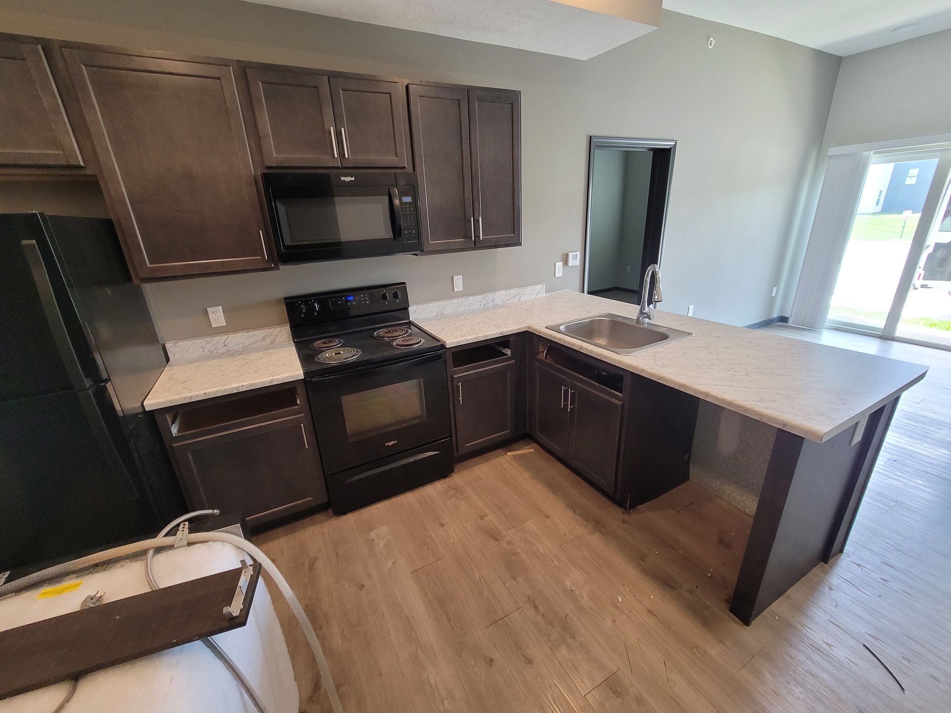 Kitchen with dark cabinets, white countertops, black appliances, and a window.