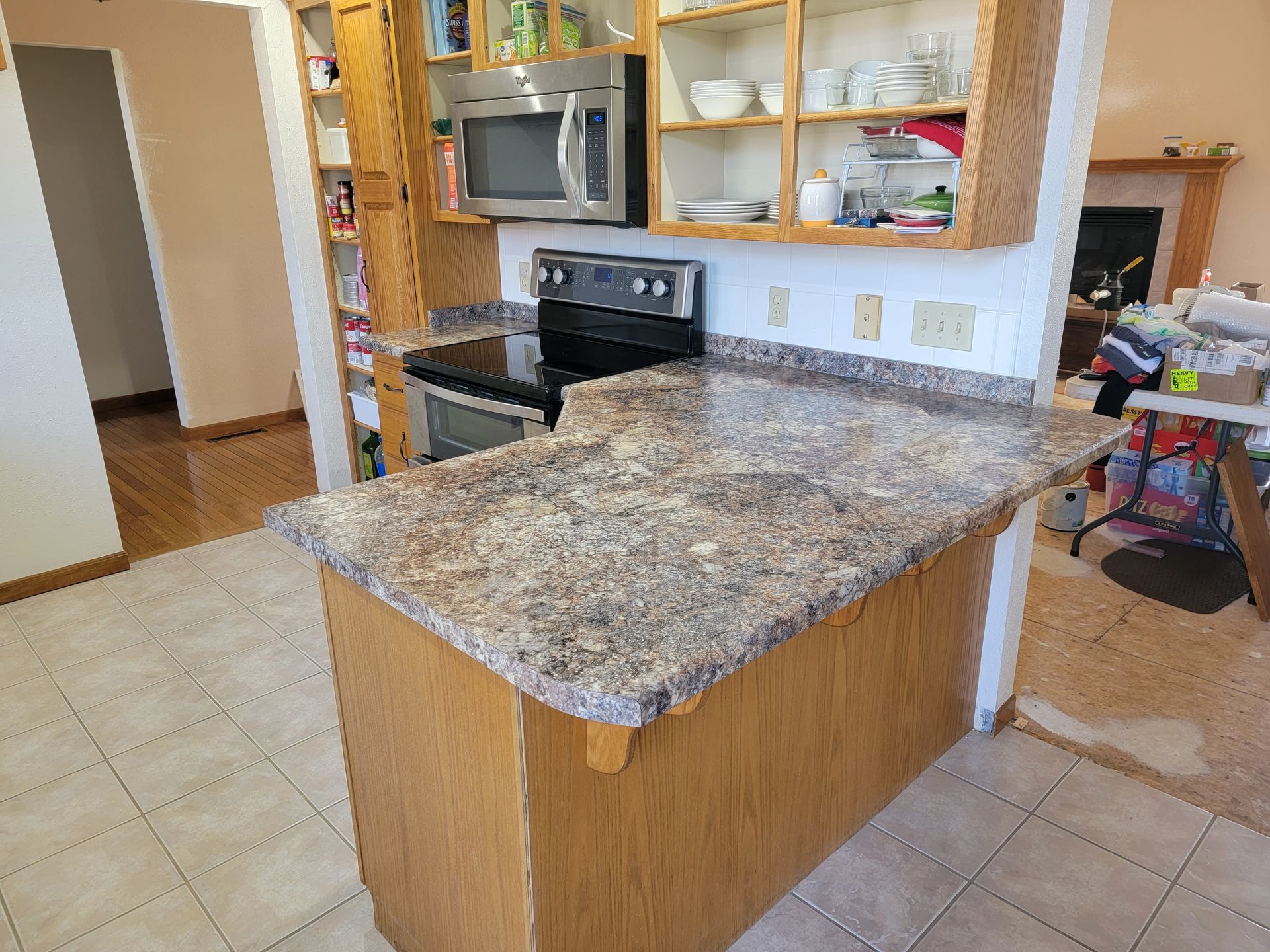 Kitchen with light-colored cabinets, countertops, and appliances. Tile floor in foreground, hardwood floor in background.