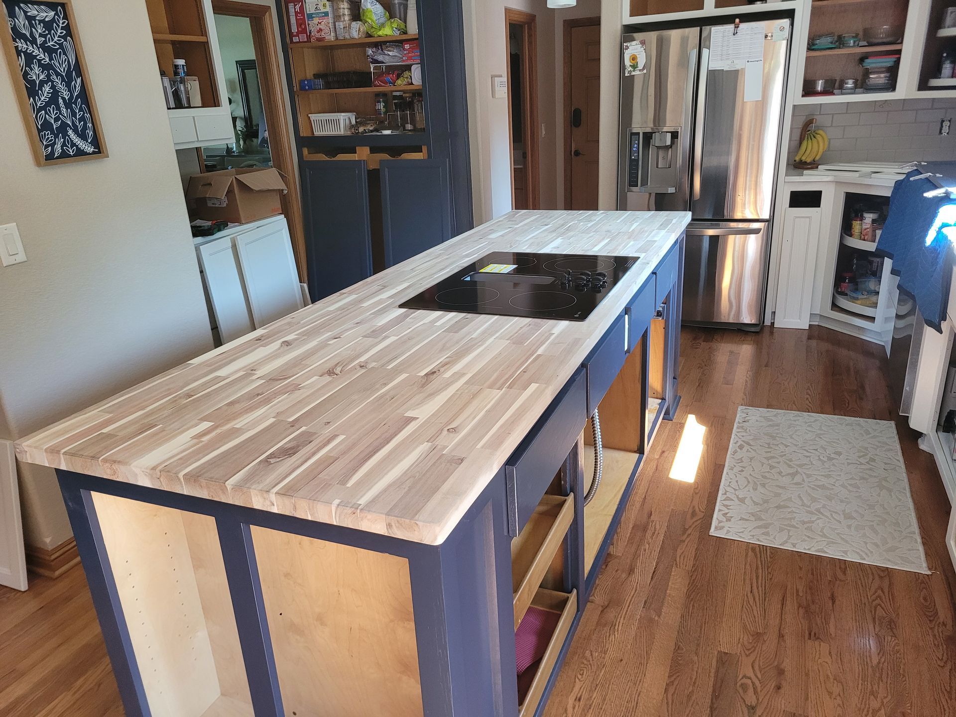 Kitchen island with a wooden countertop and blue cabinets, with a cooktop in the middle.