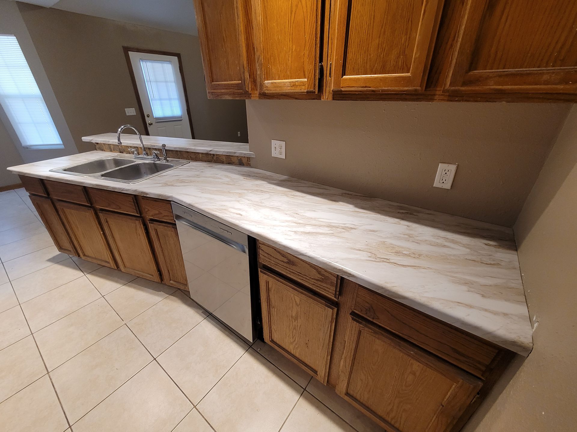 Kitchen with wooden cabinets, light countertops, stainless steel dishwasher, and sink.