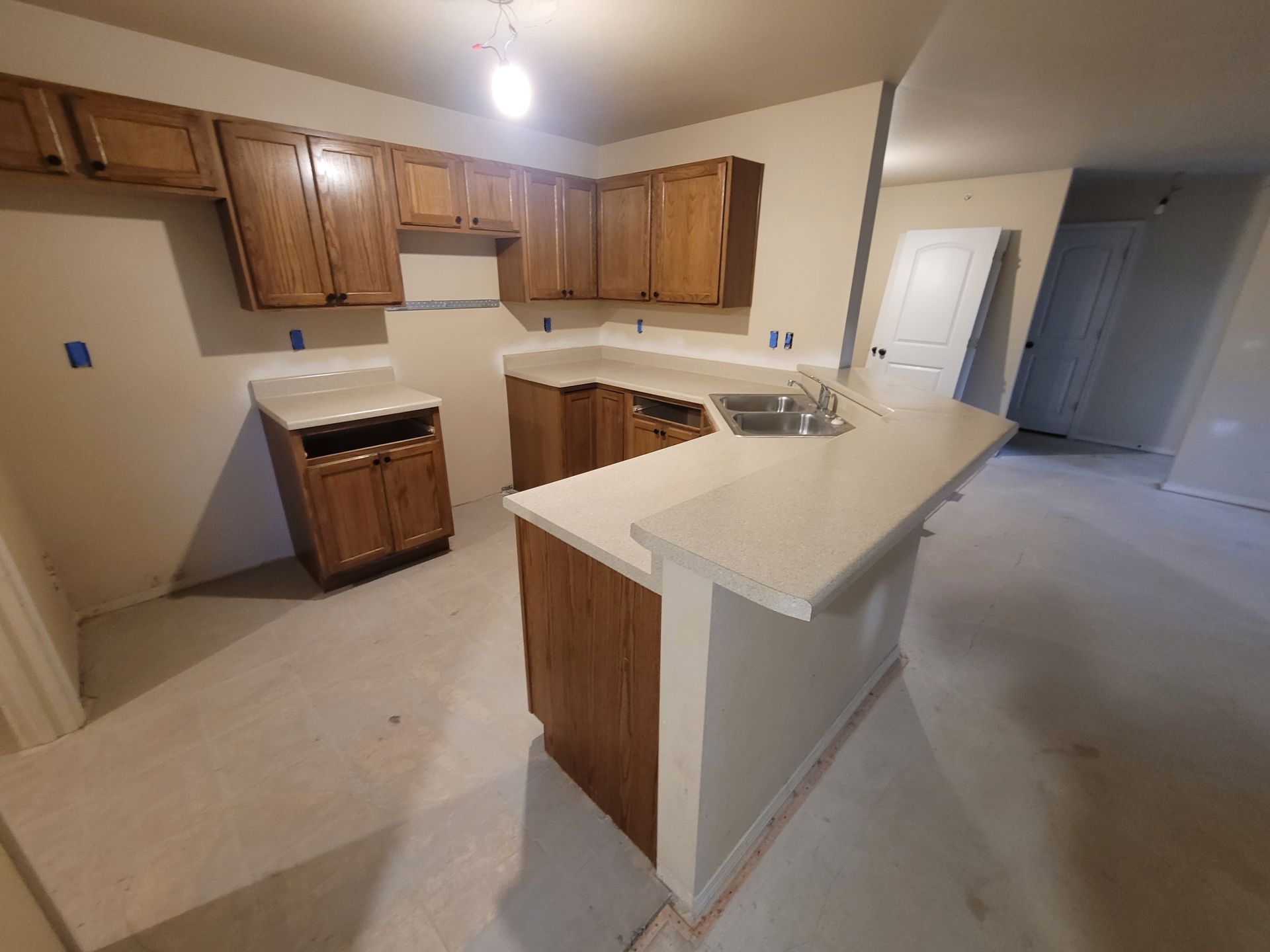 Kitchen with wooden cabinets and white countertops. Island with sink. Unfinished flooring.