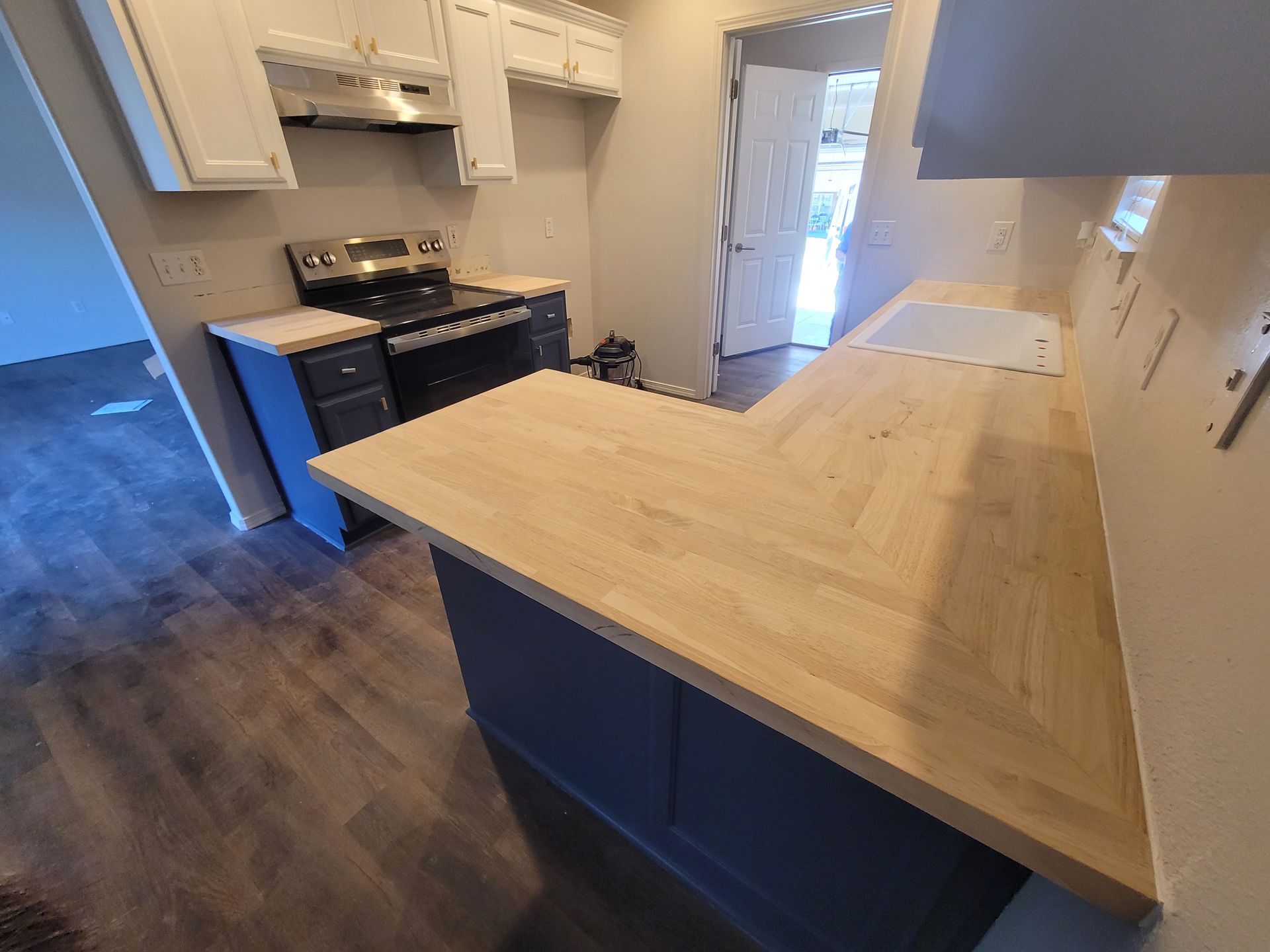 Newly renovated kitchen with dark blue cabinets, light wood countertops, and stainless steel appliances.