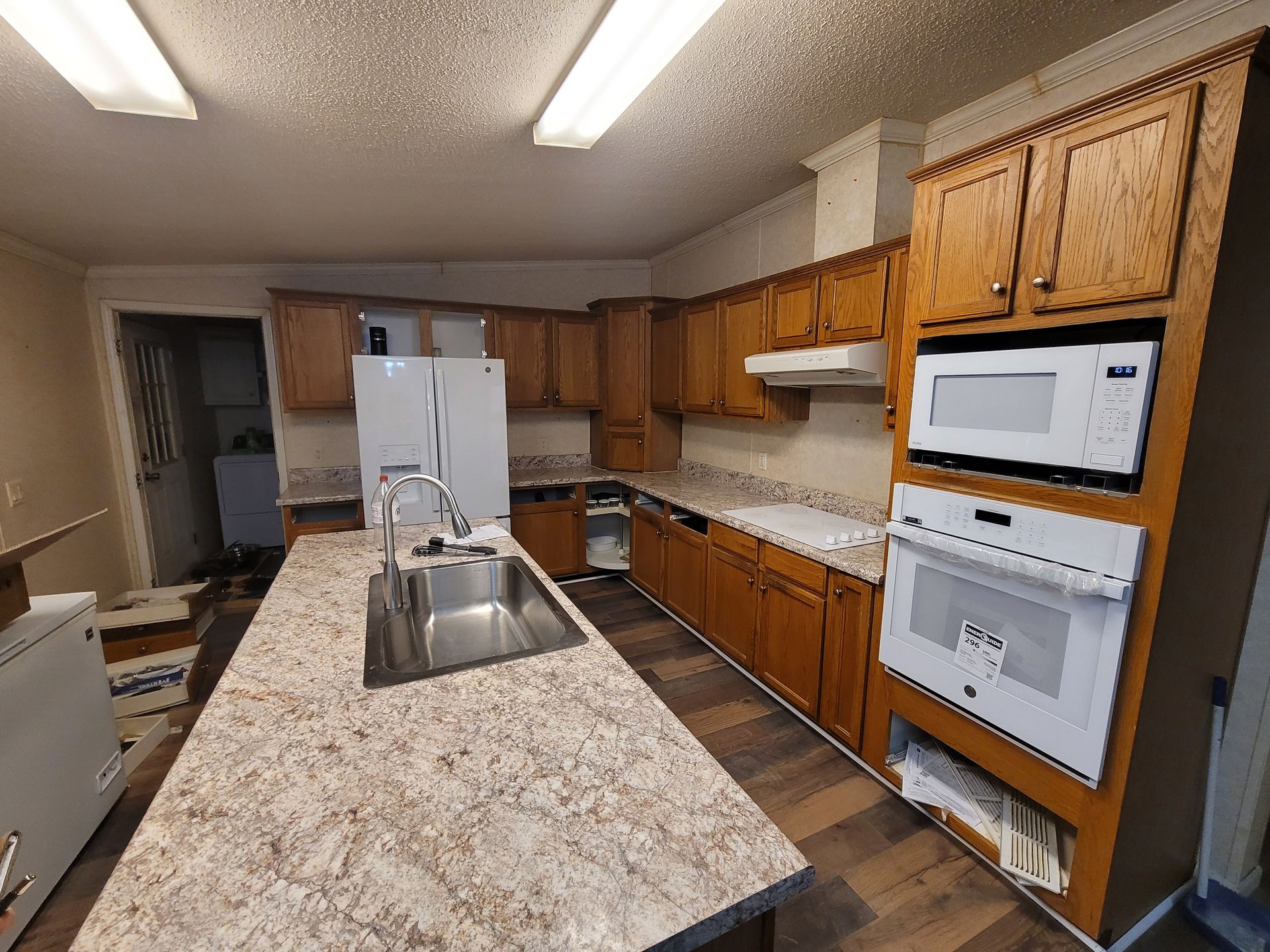 Kitchen with brown cabinets, white appliances, and a central island with a sink.