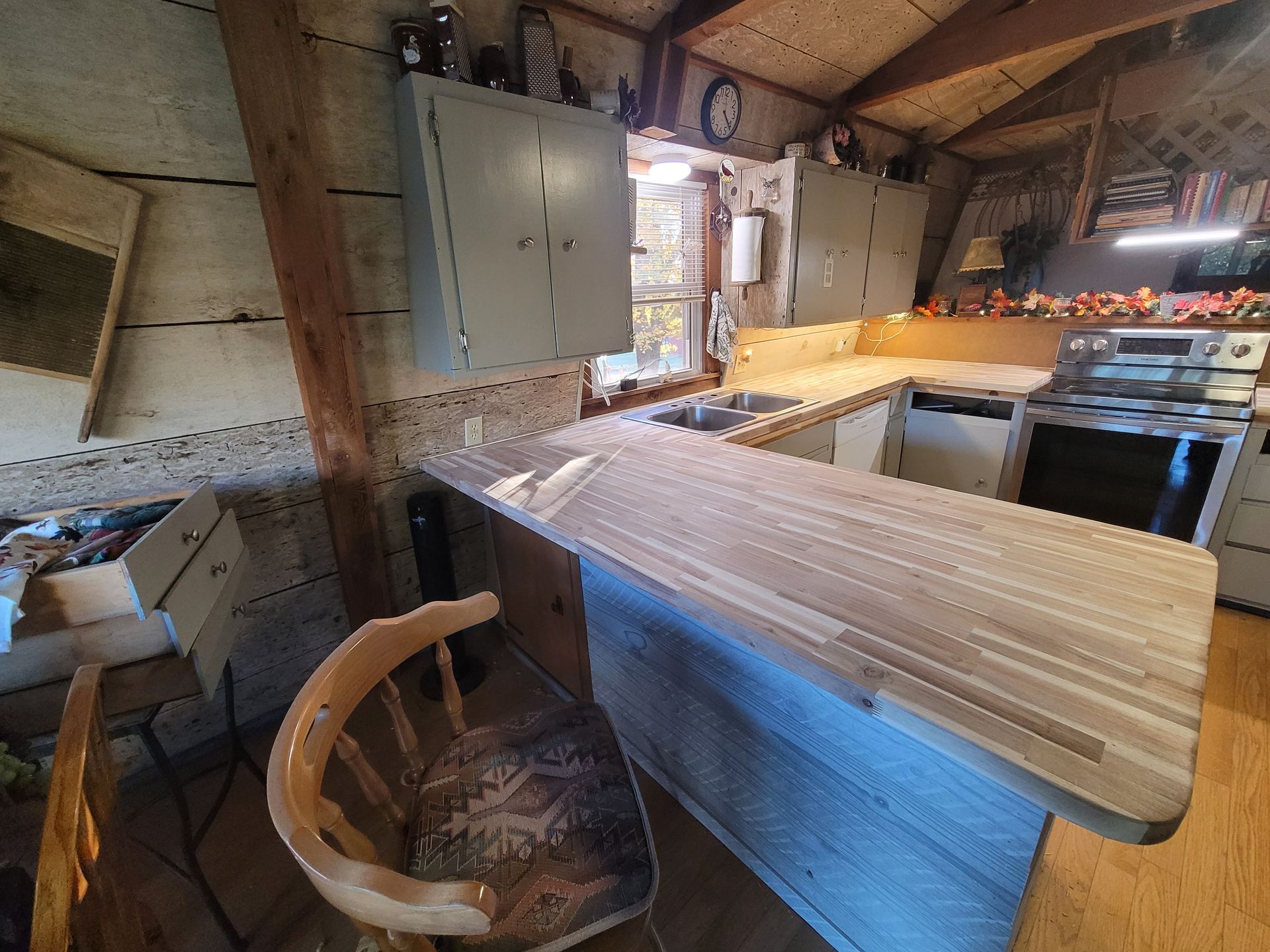 Kitchen with wooden cabinets, countertop, and a wooden chair. Sunlight streams in from a window.