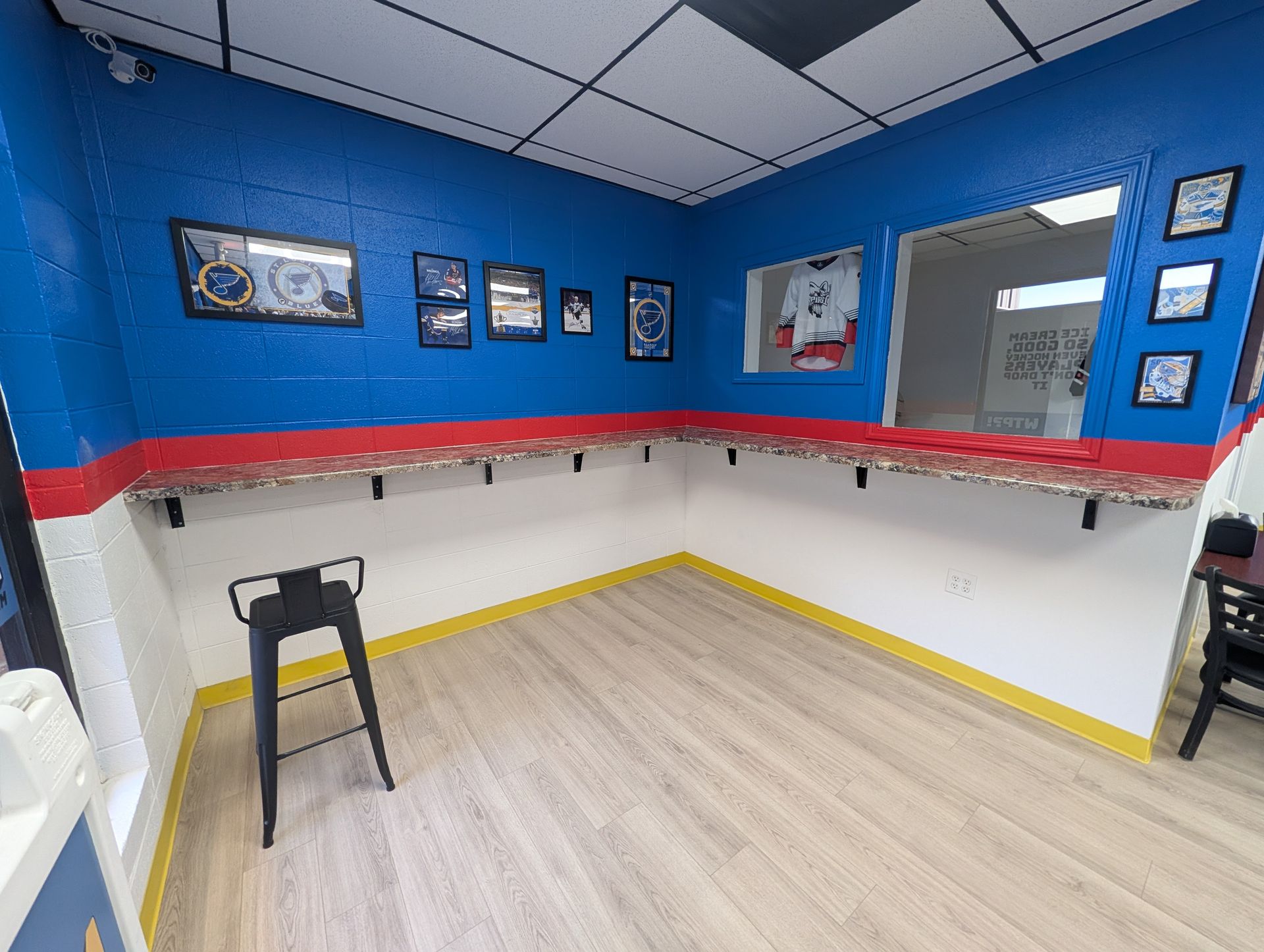 Blue and white room with a counter and stools, decorated with framed images, and a window.