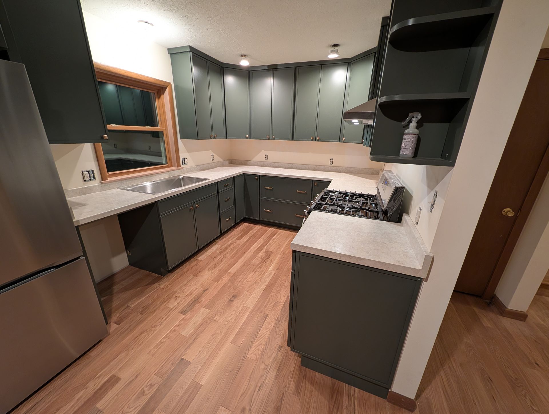 Dark green kitchen cabinets with white countertops and wood flooring.