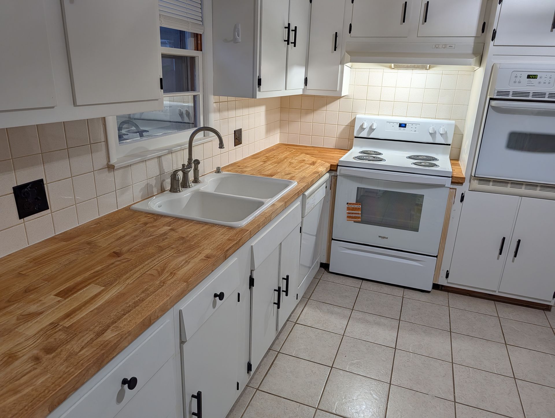 White kitchen with wood countertops, white appliances, and tiled backsplash and floor.