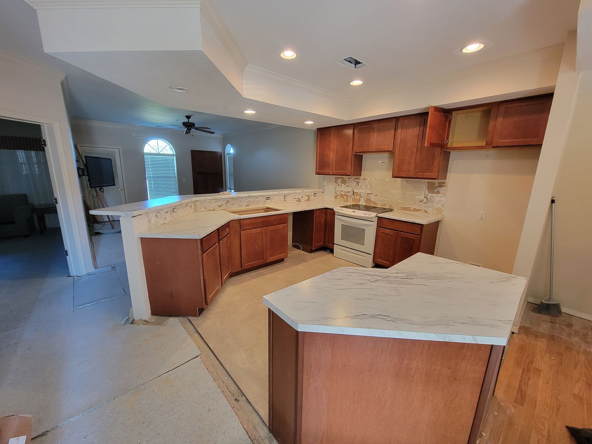 Renovated kitchen with brown cabinets, white countertops, and white appliances; open to another room.