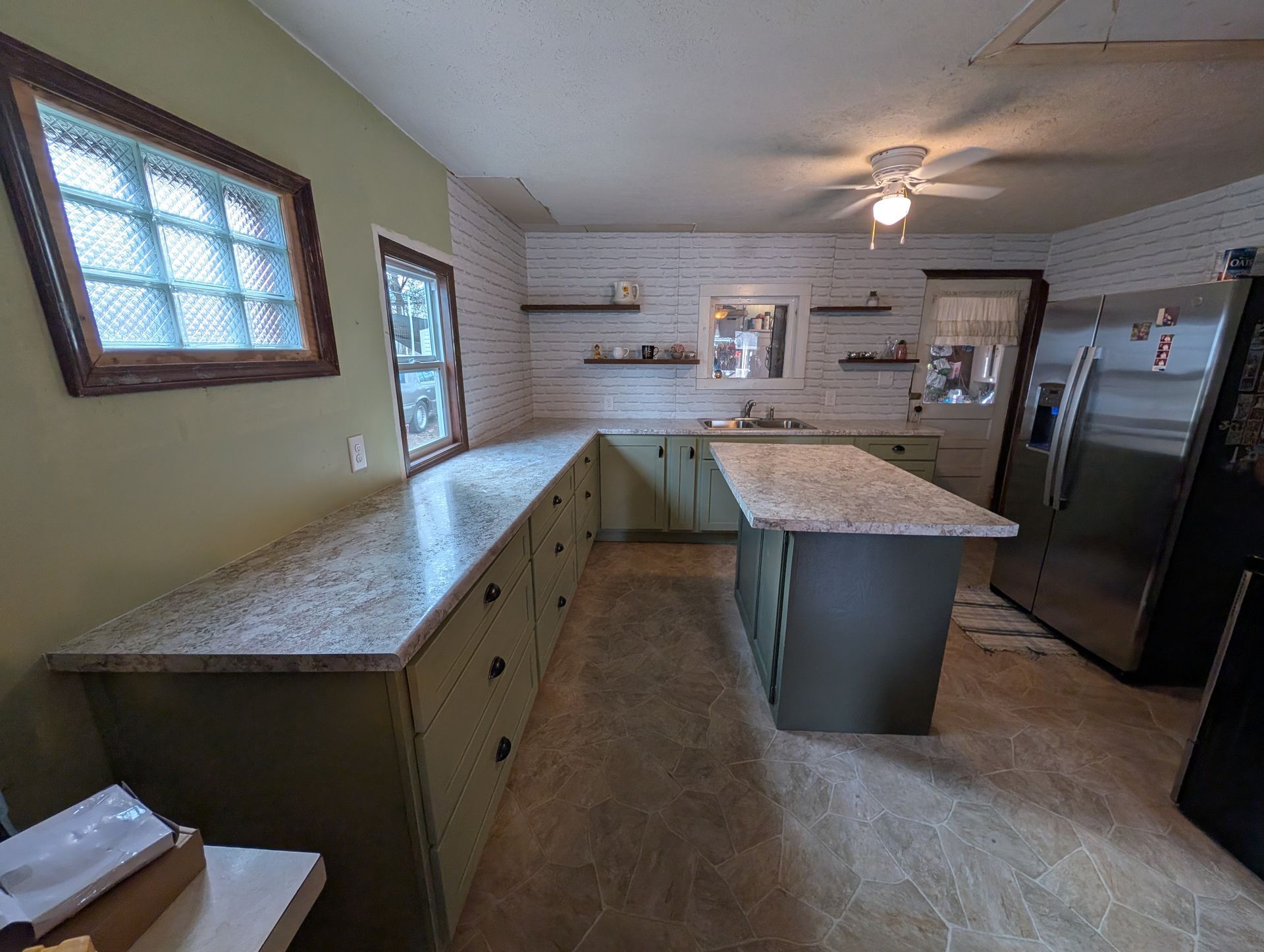 Kitchen with olive-green cabinets, granite countertops, an island, and a stainless steel refrigerator.