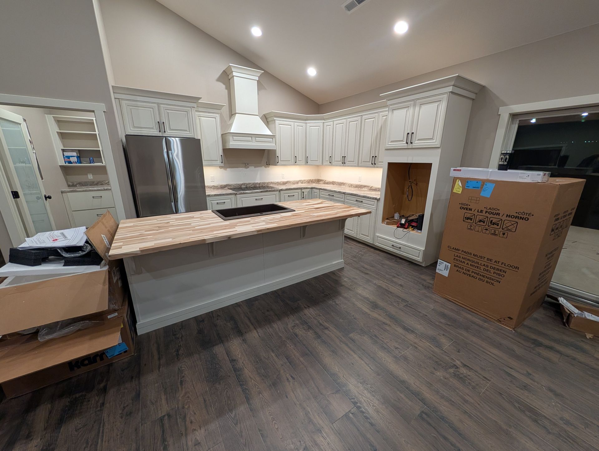 Kitchen renovation in progress: white cabinets, island with countertop, stainless steel refrigerator, boxes on the floor.