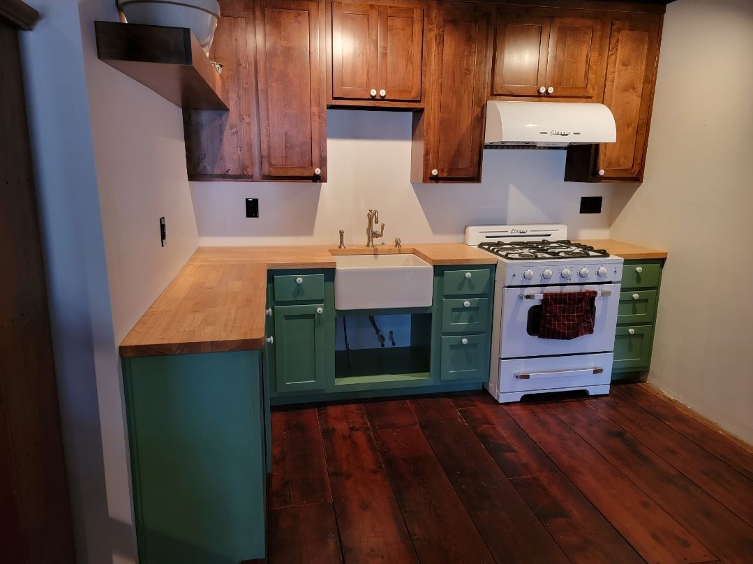 Small kitchen with green cabinets, wooden countertops, dark wood floor, and white range.