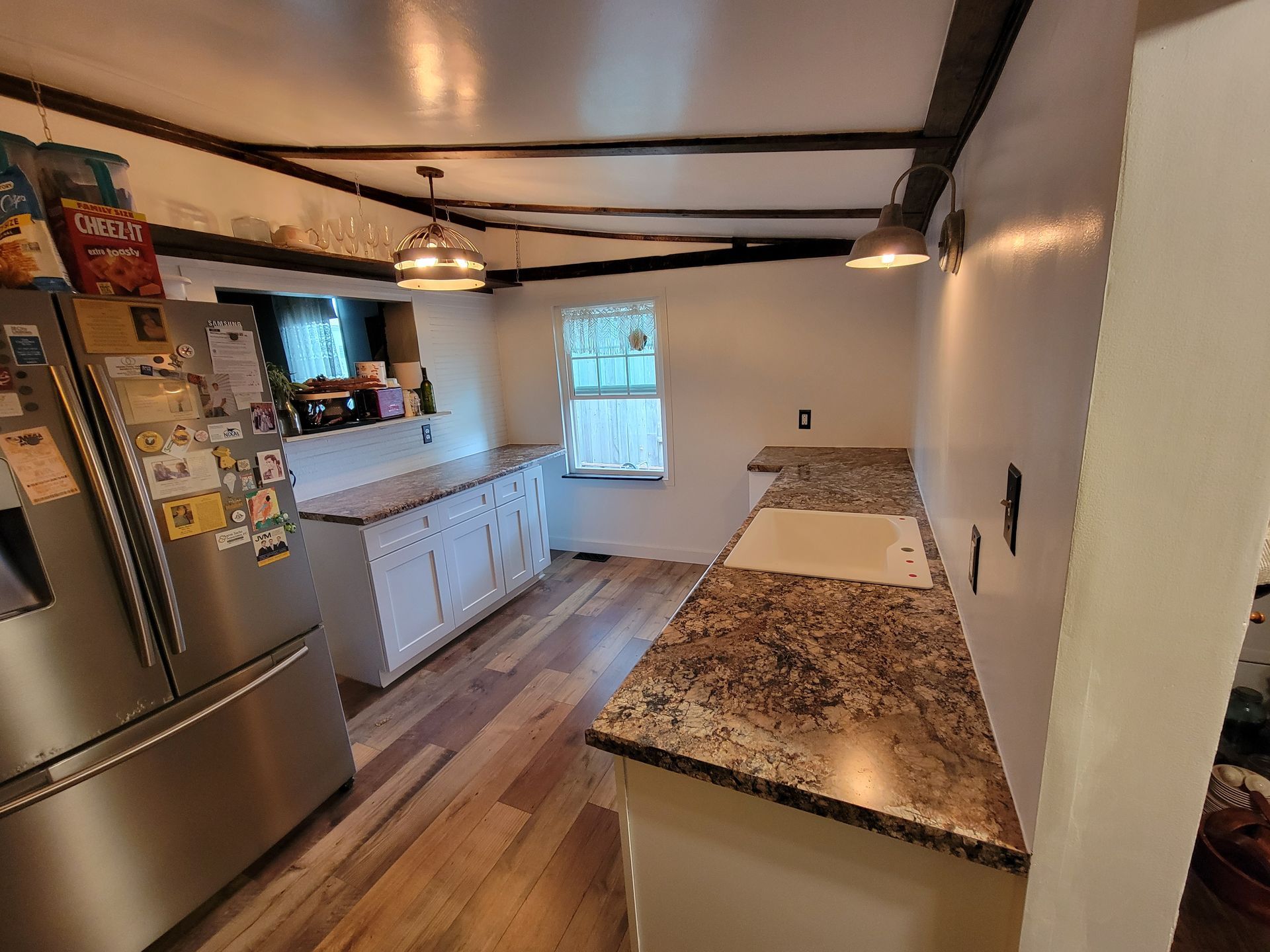 Kitchen with white cabinets, wood floor, granite countertops, and stainless steel refrigerator.
